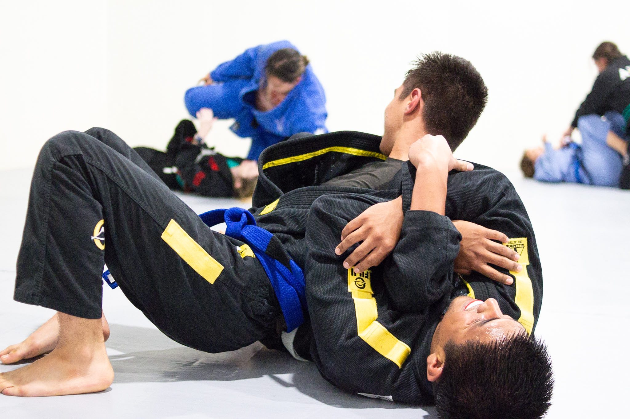 Two teen jiu-jitsu students in yellow belts drilling a cross-choke from closed guard