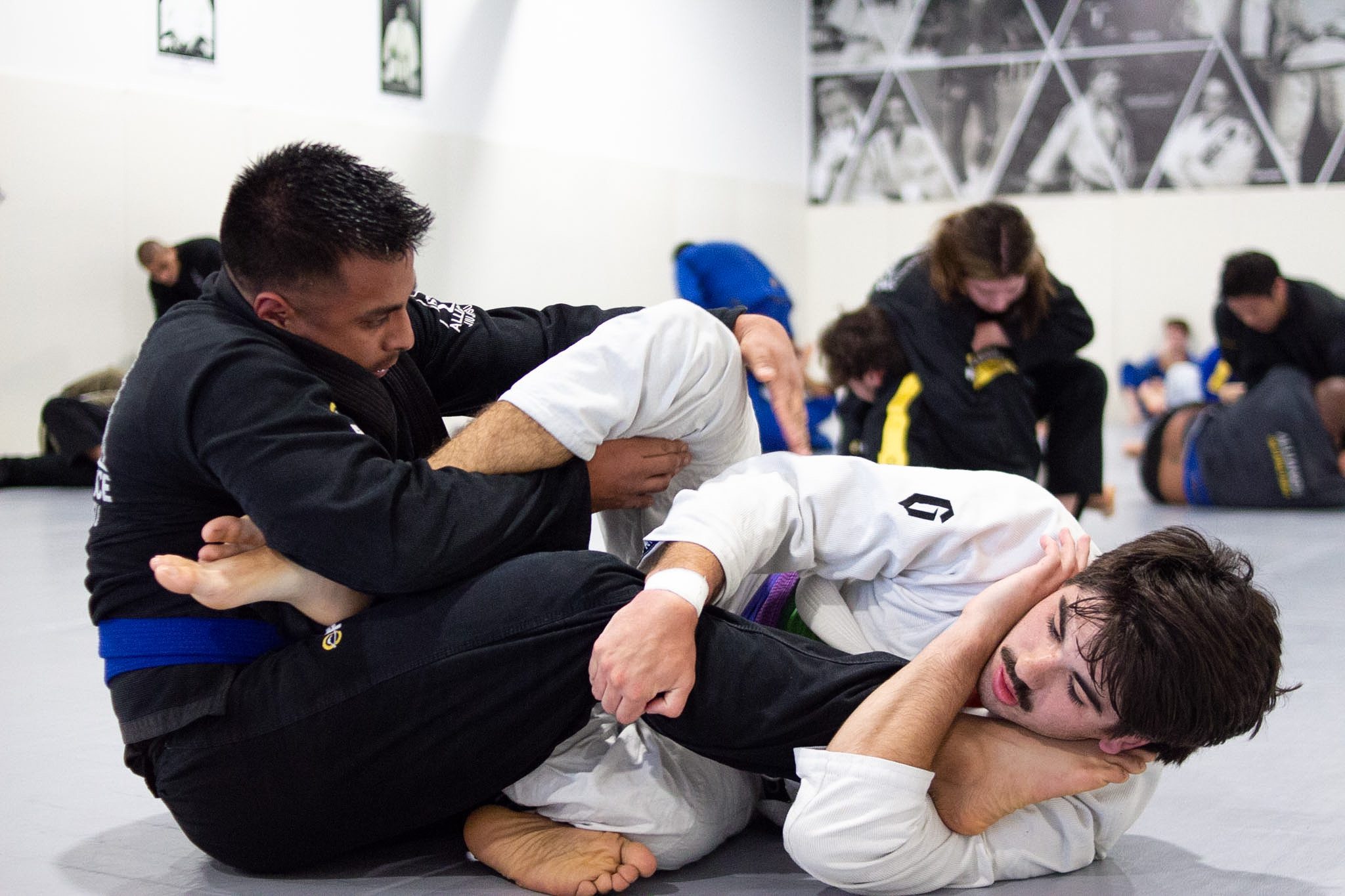 Coach guiding a teen student through a closed-guard breakdown during jiu-jitsu class