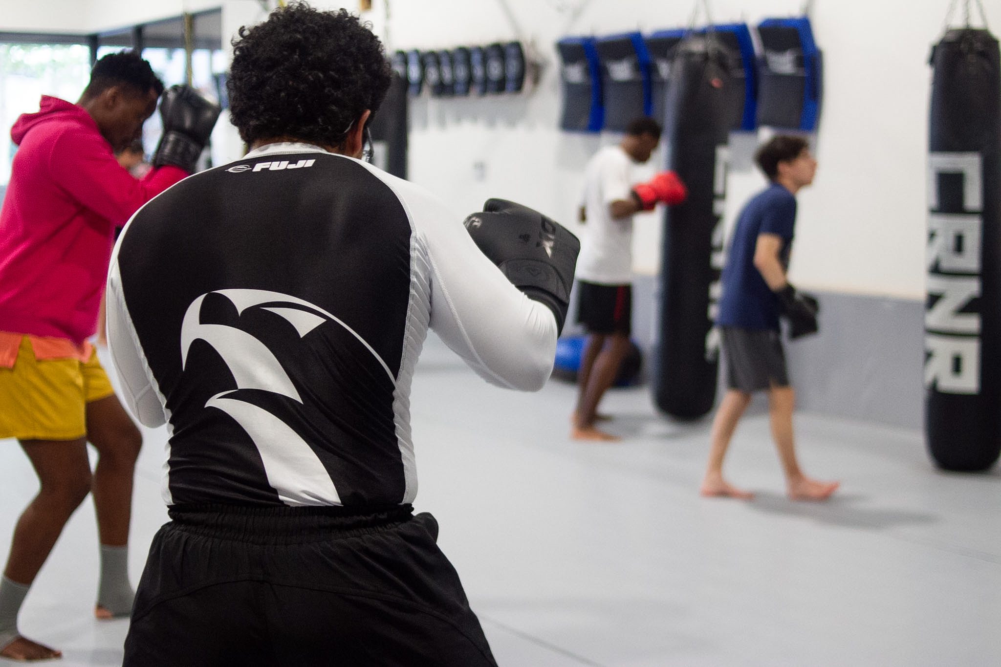 Adult kickboxing student drilling shadow work with heavy bags in background