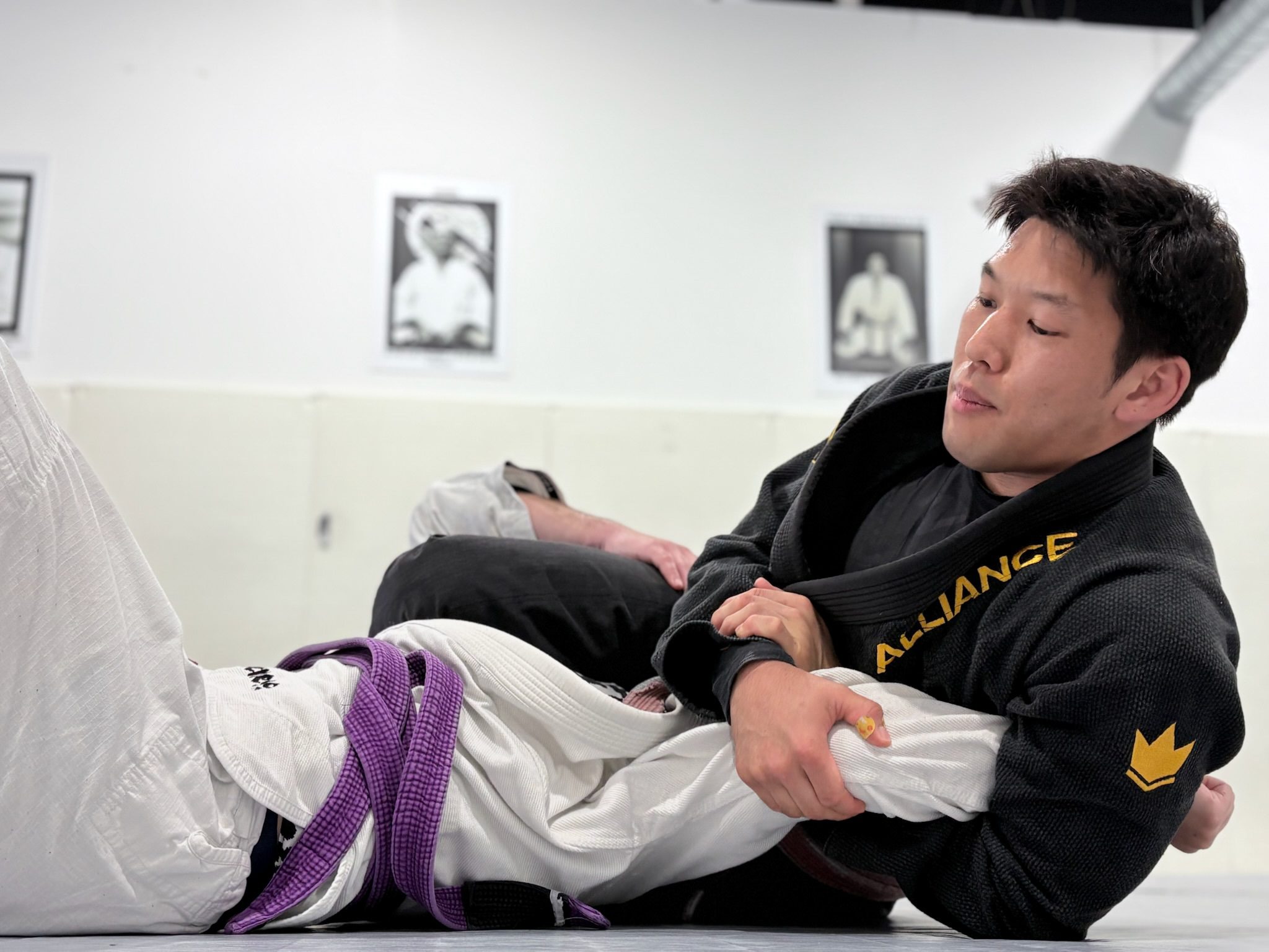 Purple belt grappler controlling an opponent's leg from guard during advanced jiu-jitsu drilling