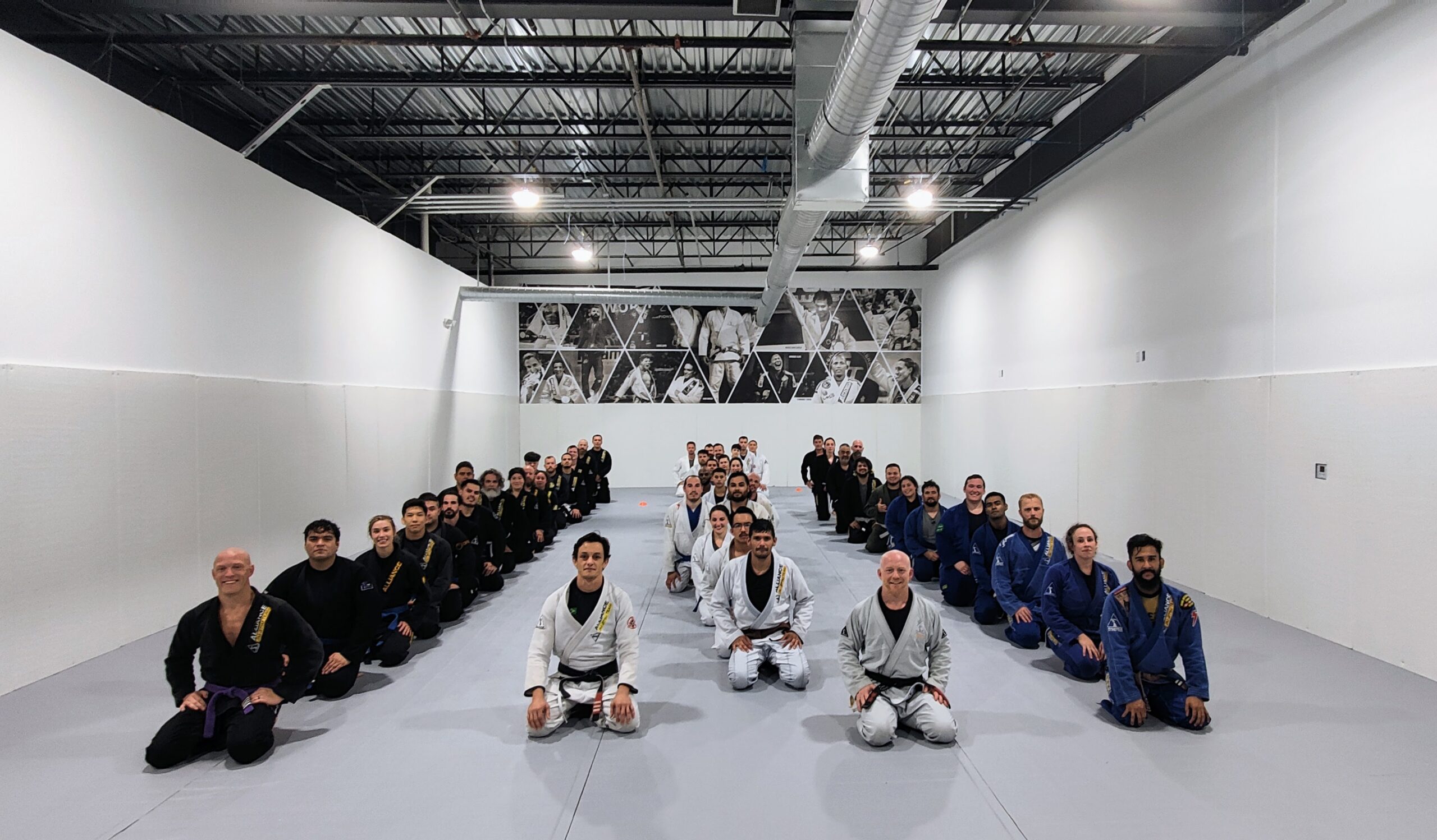 Adult BJJ students kneeling in formation across the mats after class