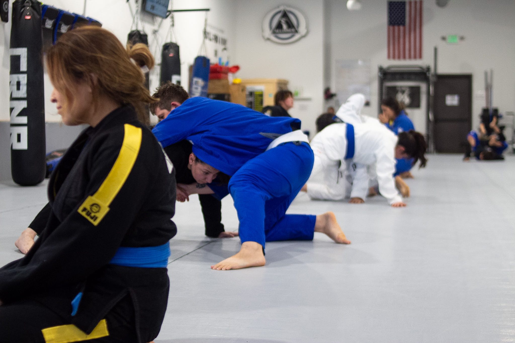 Adult BJJ class running warm-up movement drills across the mat