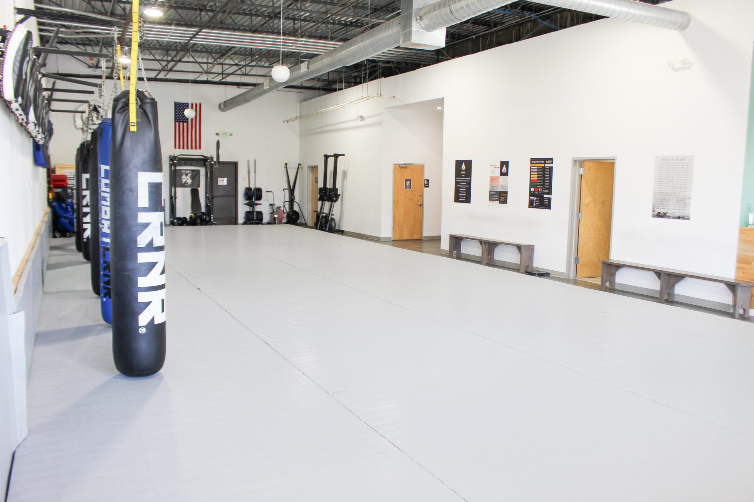 Long mat lined with heavy bags, conditioning sled, and benches along the back wall
