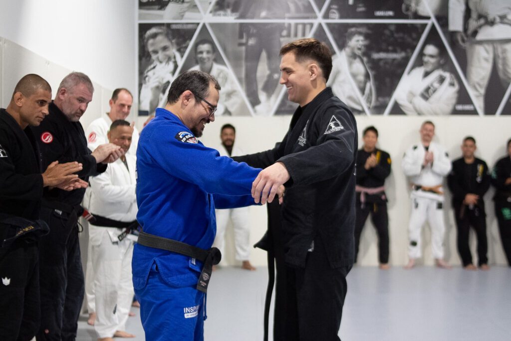 Ed Ramos in a blue gi shaking hands with Thomas Dougherty during a black belt promotion