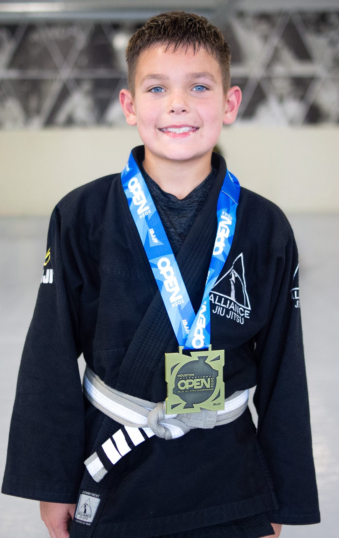 Young Junior Eagles student in black Alliance gi proudly wearing his tournament medal