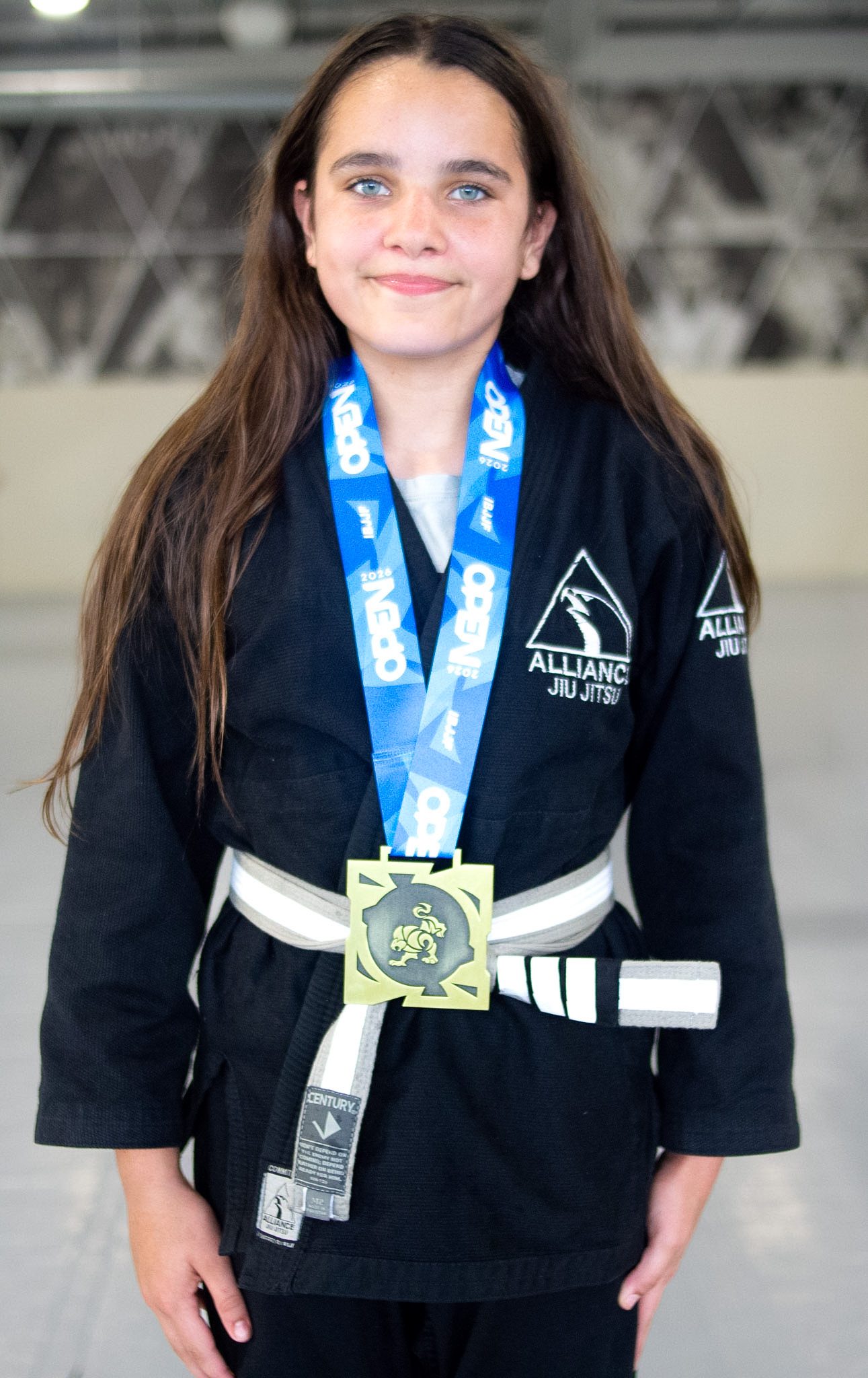 Young girl in Alliance gi wearing a gold medal after winning her division