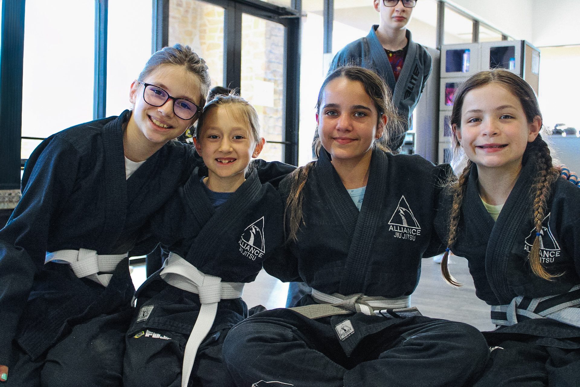 Four white-belt kids in Alliance gis smiling for a class photo