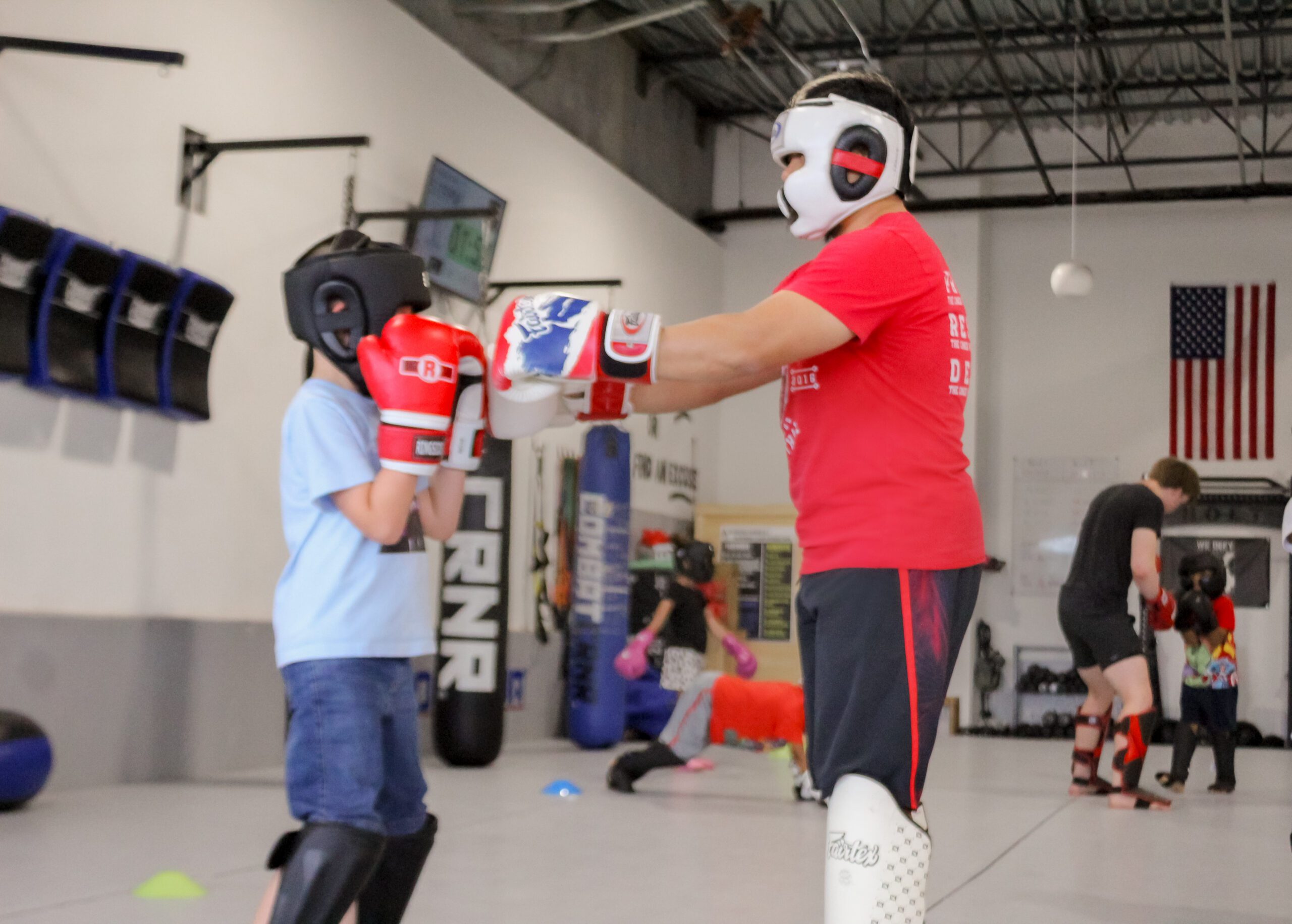 Young Muay Thai student in headgear practicing partner padwork with a coach
