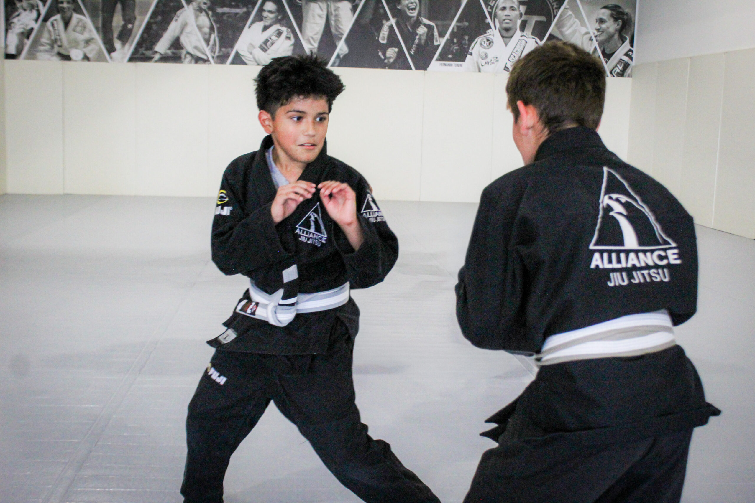 Two young Alliance students in white belts drilling stand-up grips during kids class