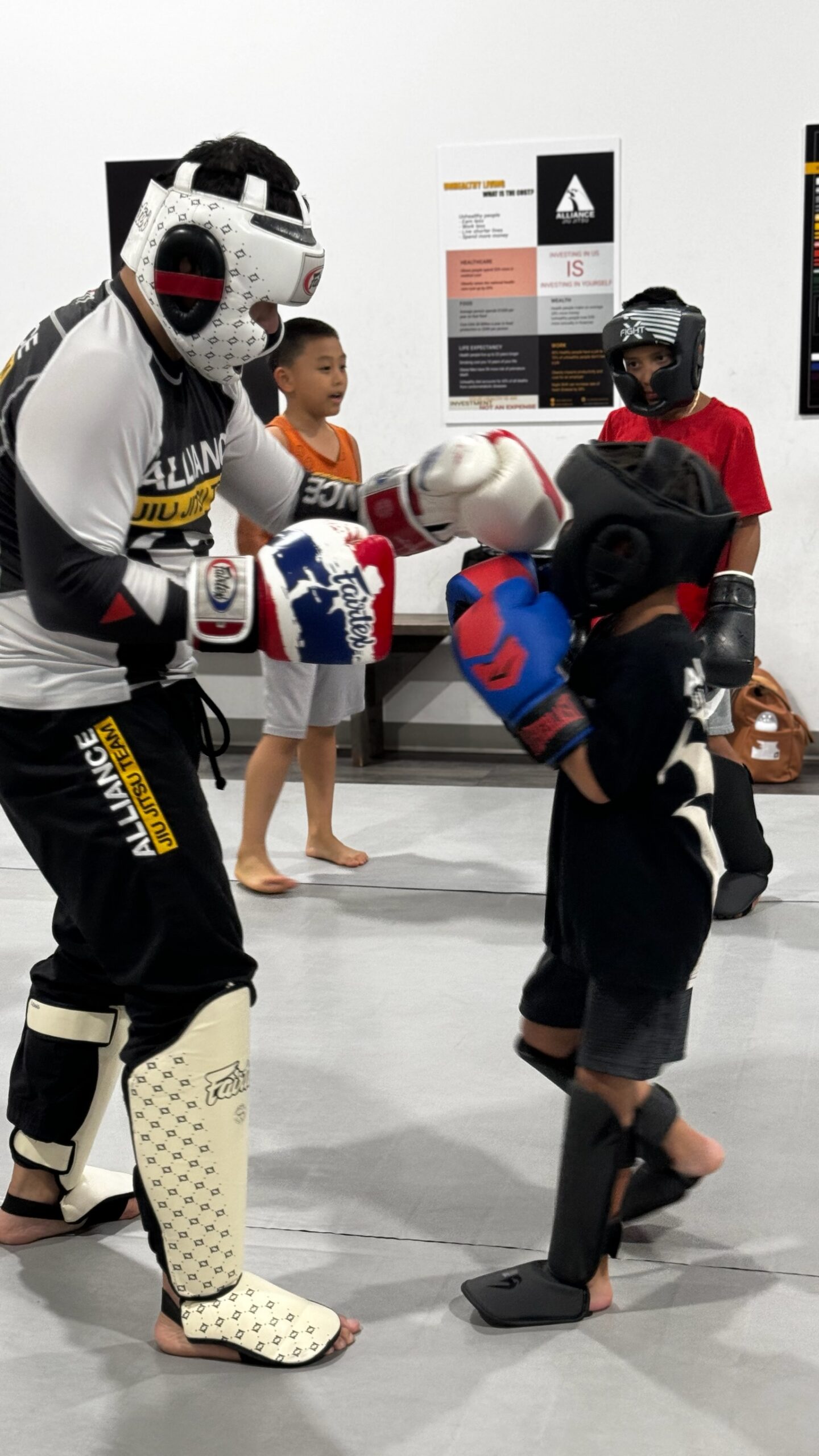 Coach in shin guards working partner padwork with two young Muay Thai students