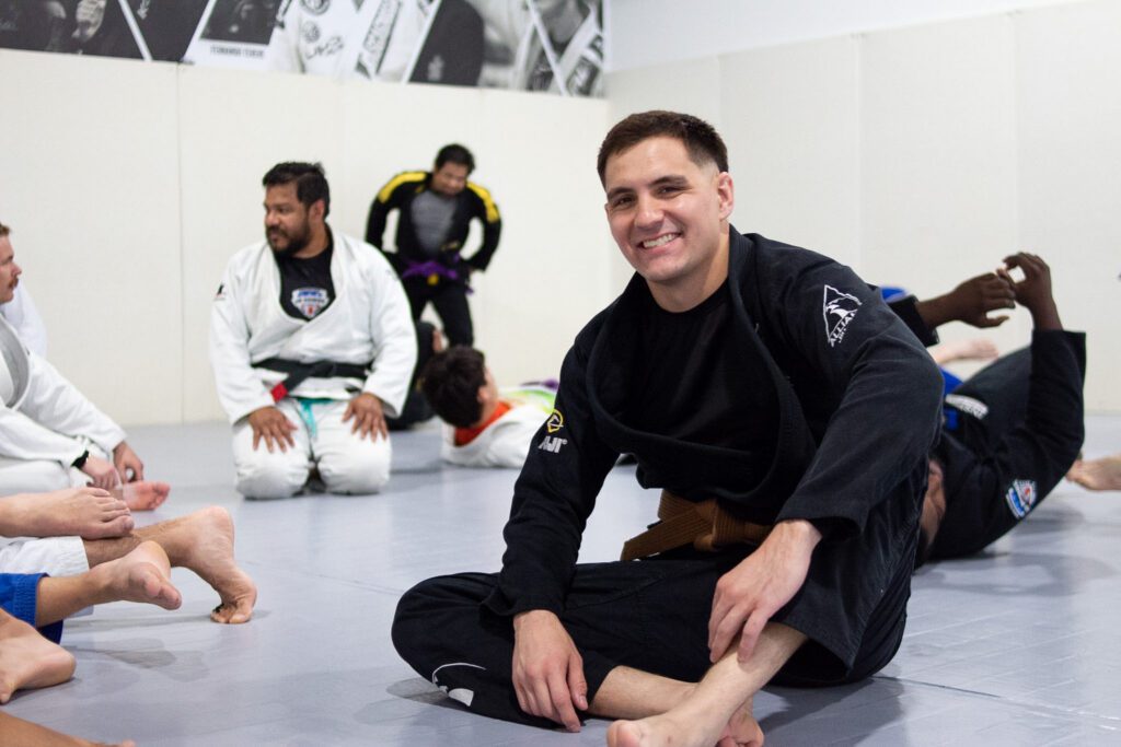 Three Alliance BJJ teammates in gis throwing shakas after a belt promotion ceremony