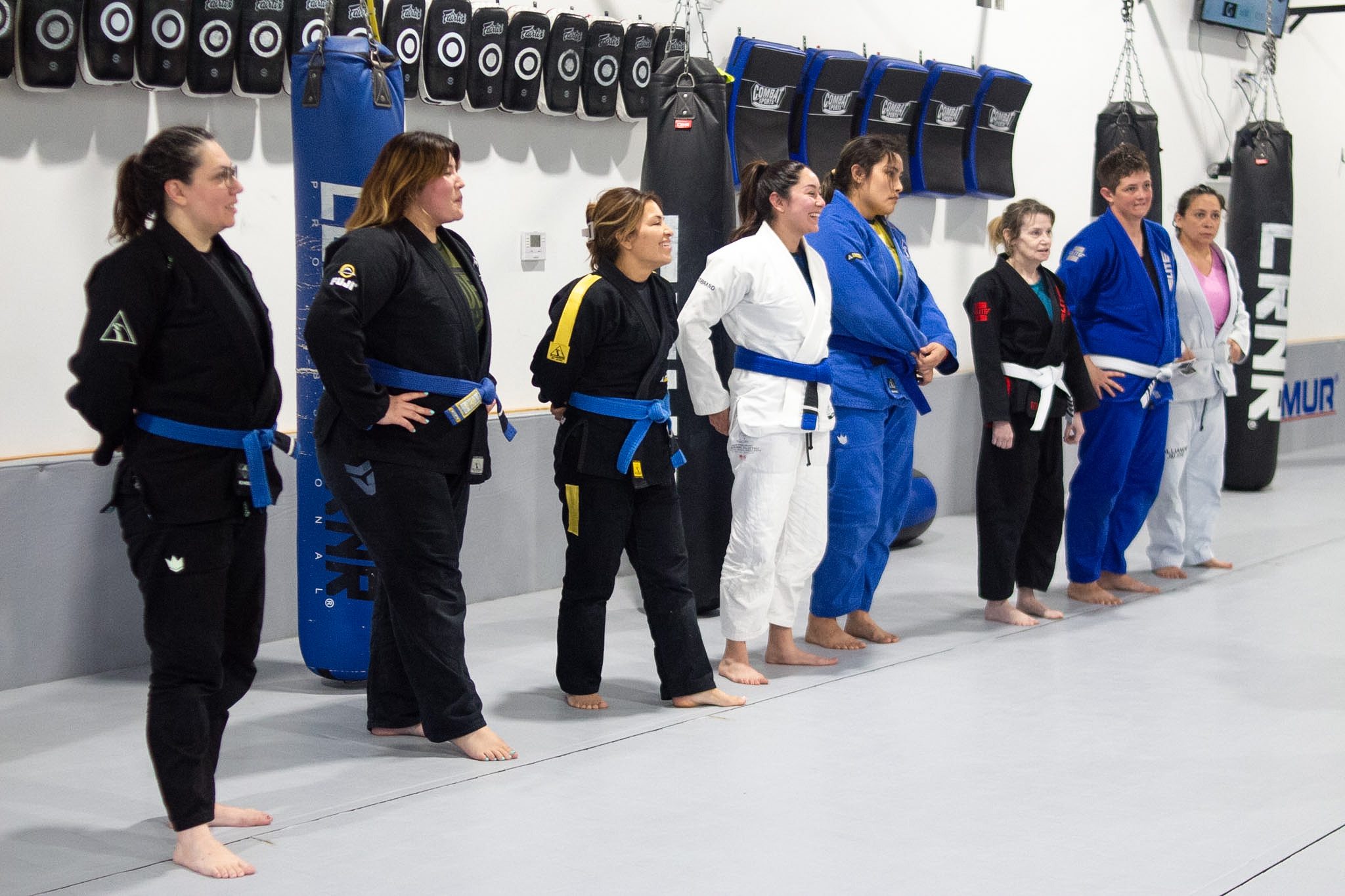 Eight women from various belt ranks lined up before jiu-jitsu class