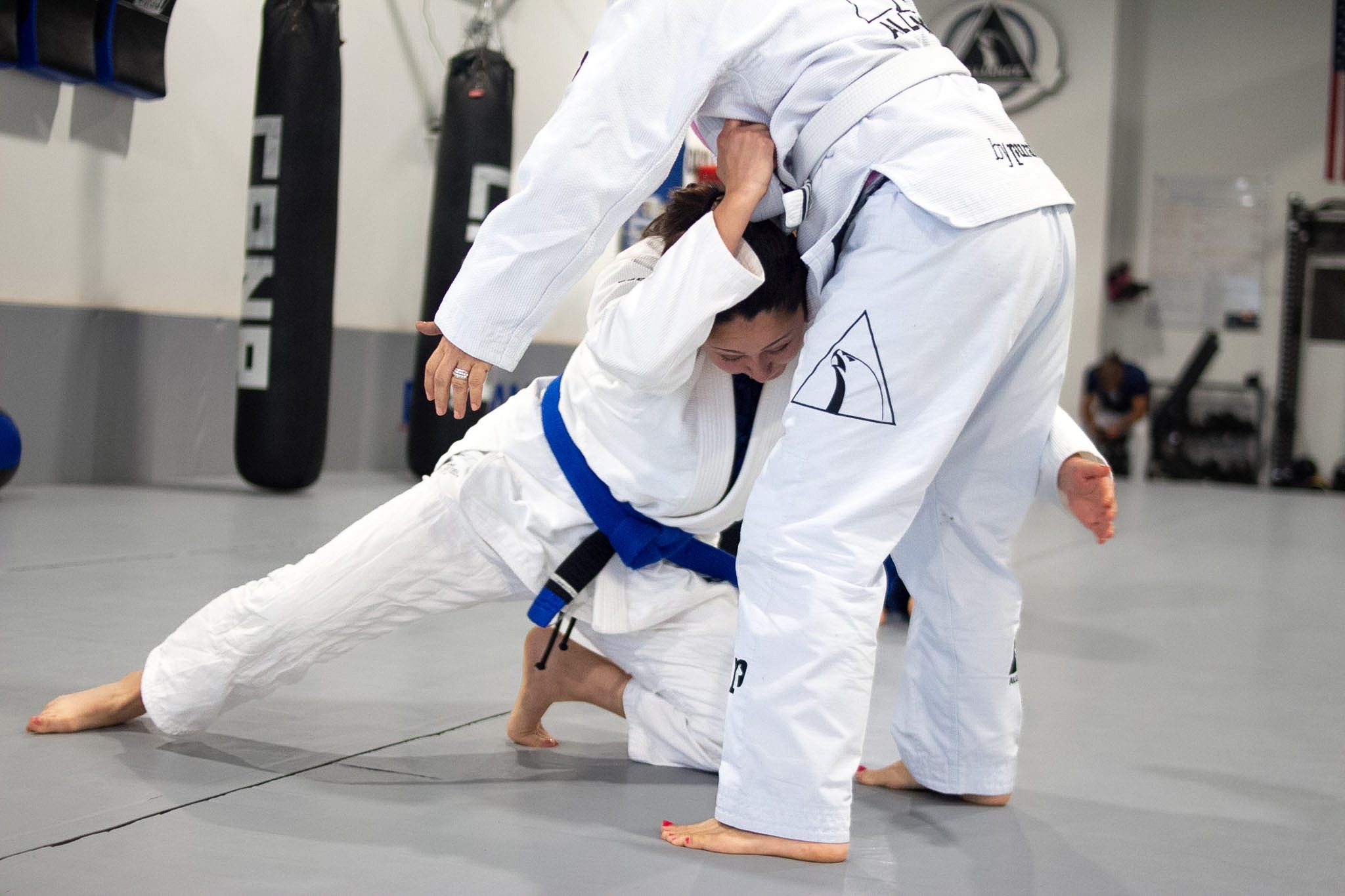 Blue belt woman driving a takedown on her training partner during Brazilian jiu-jitsu class