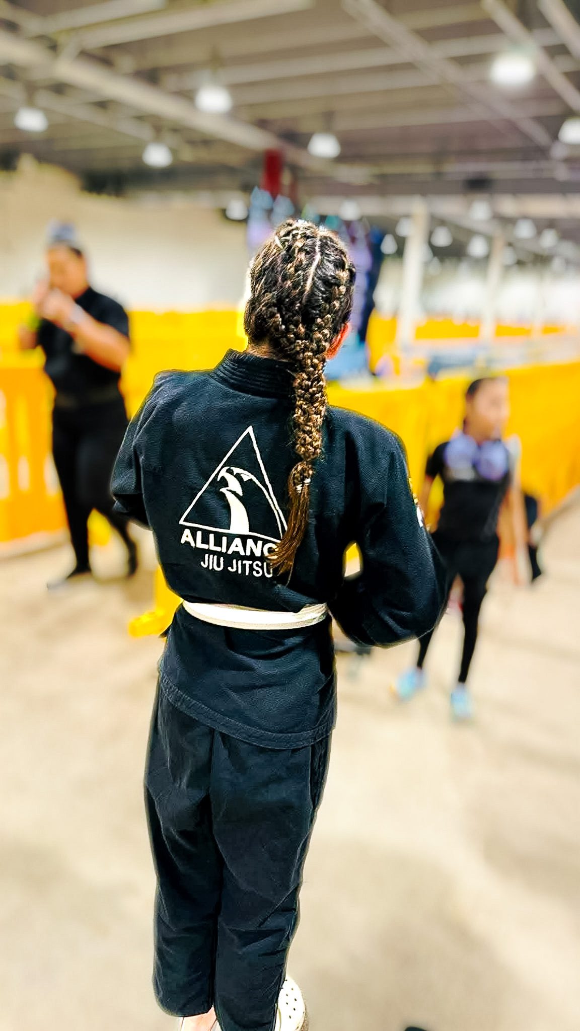 Young Alliance Jiu-Jitsu competitor with braided hair walking into the tournament area