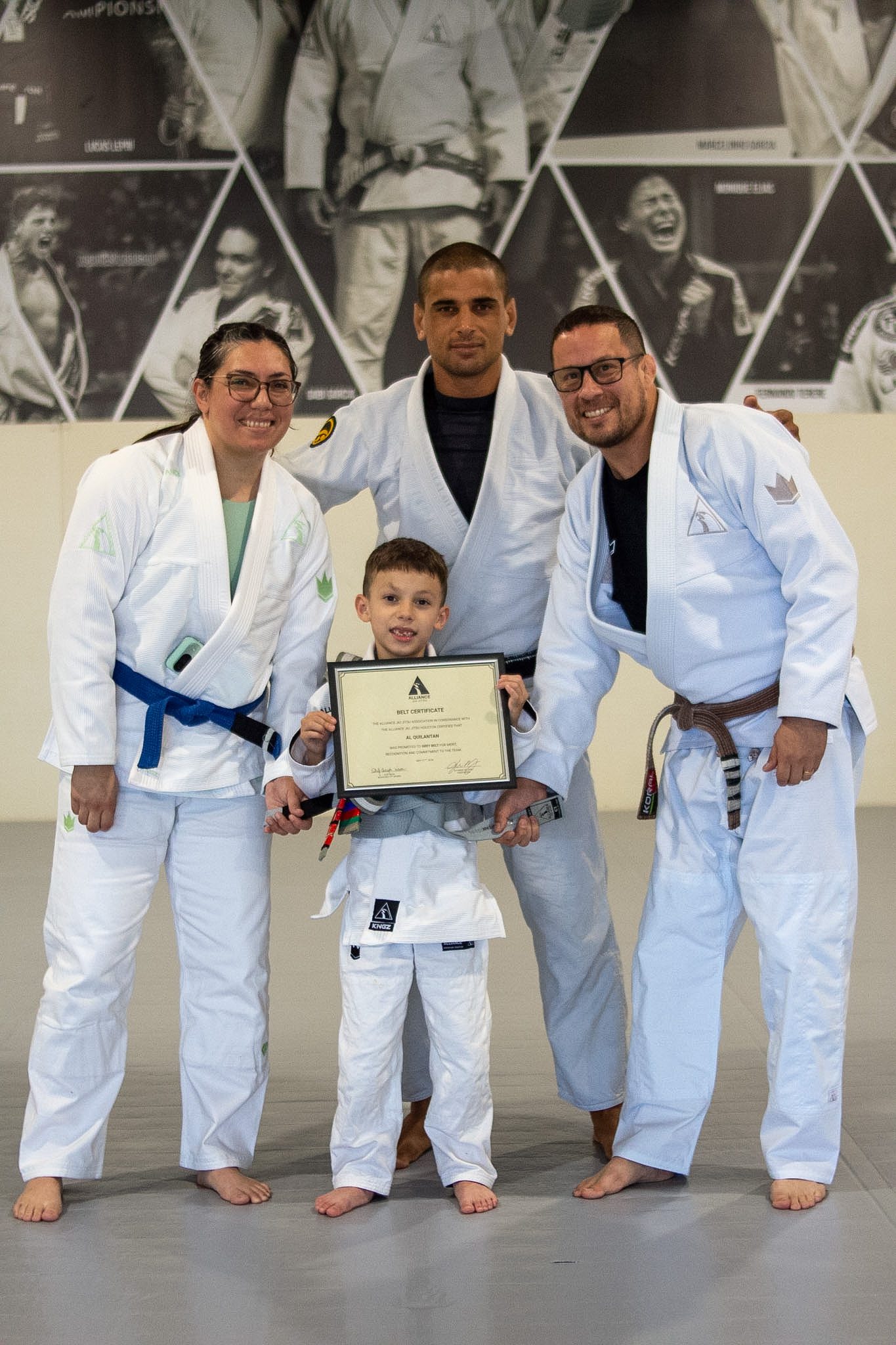 Newly promoted student holds Alliance belt certificate beside three coaches