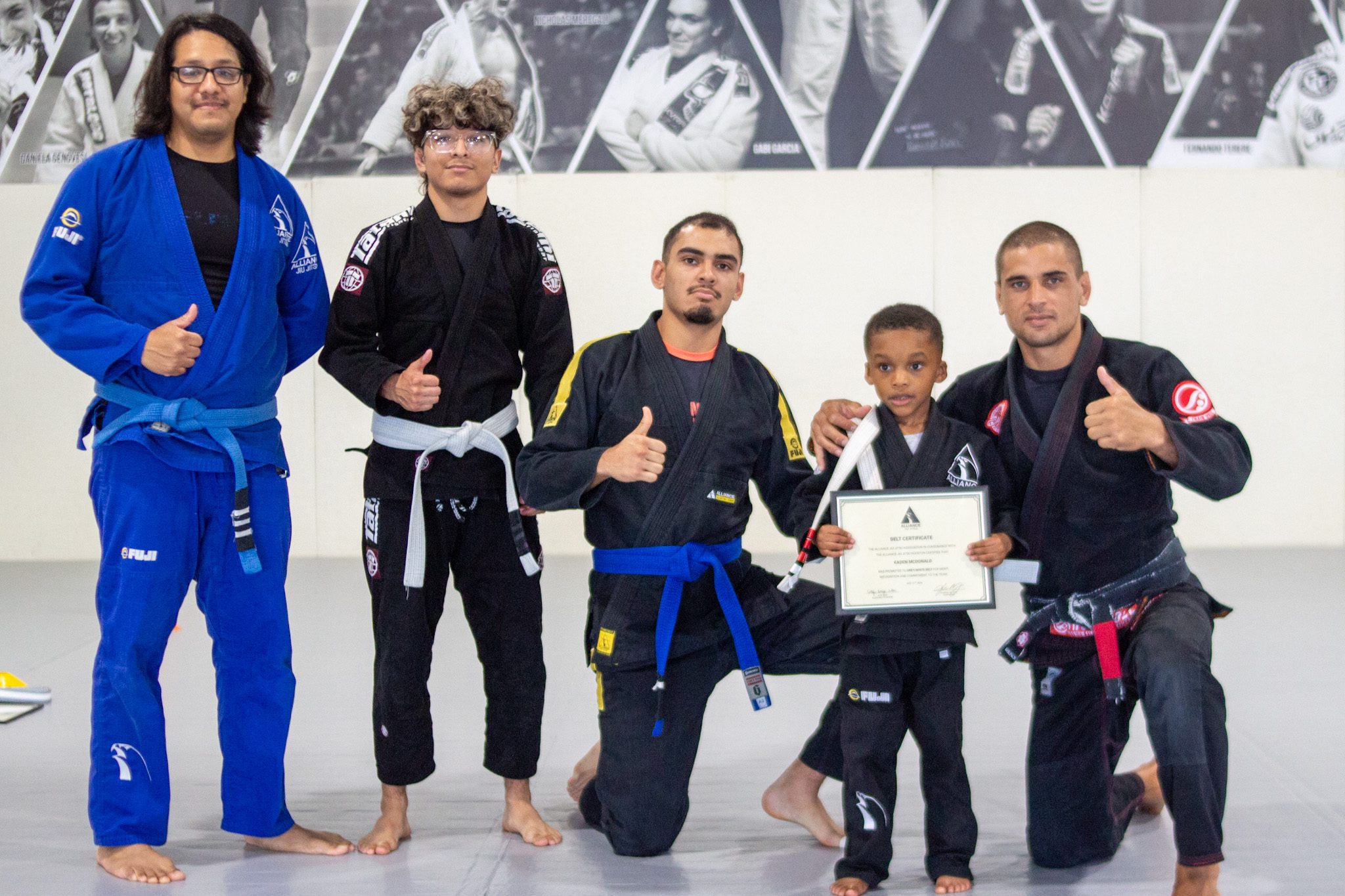 Five Alliance jiu-jitsu coaches gather around a small promoted Tiny Eagle