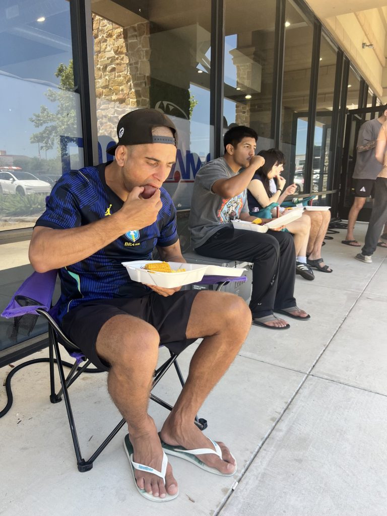 Member in Jordan shirt eating crawfish and corn from a takeout container outside