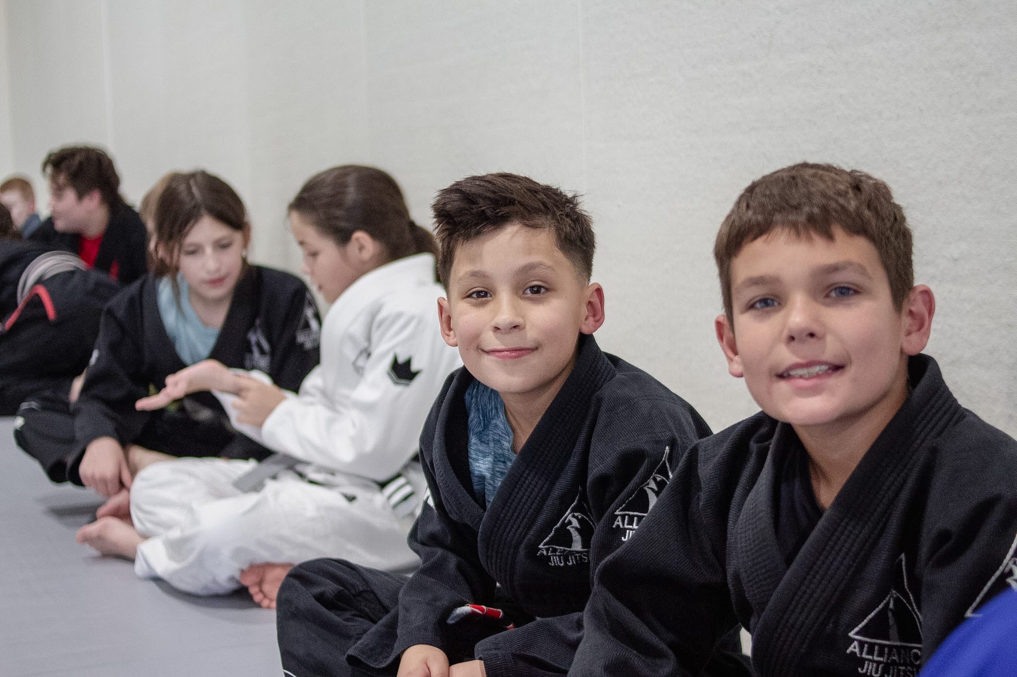 Two Alliance students in green and black gis drill grip fighting from standing