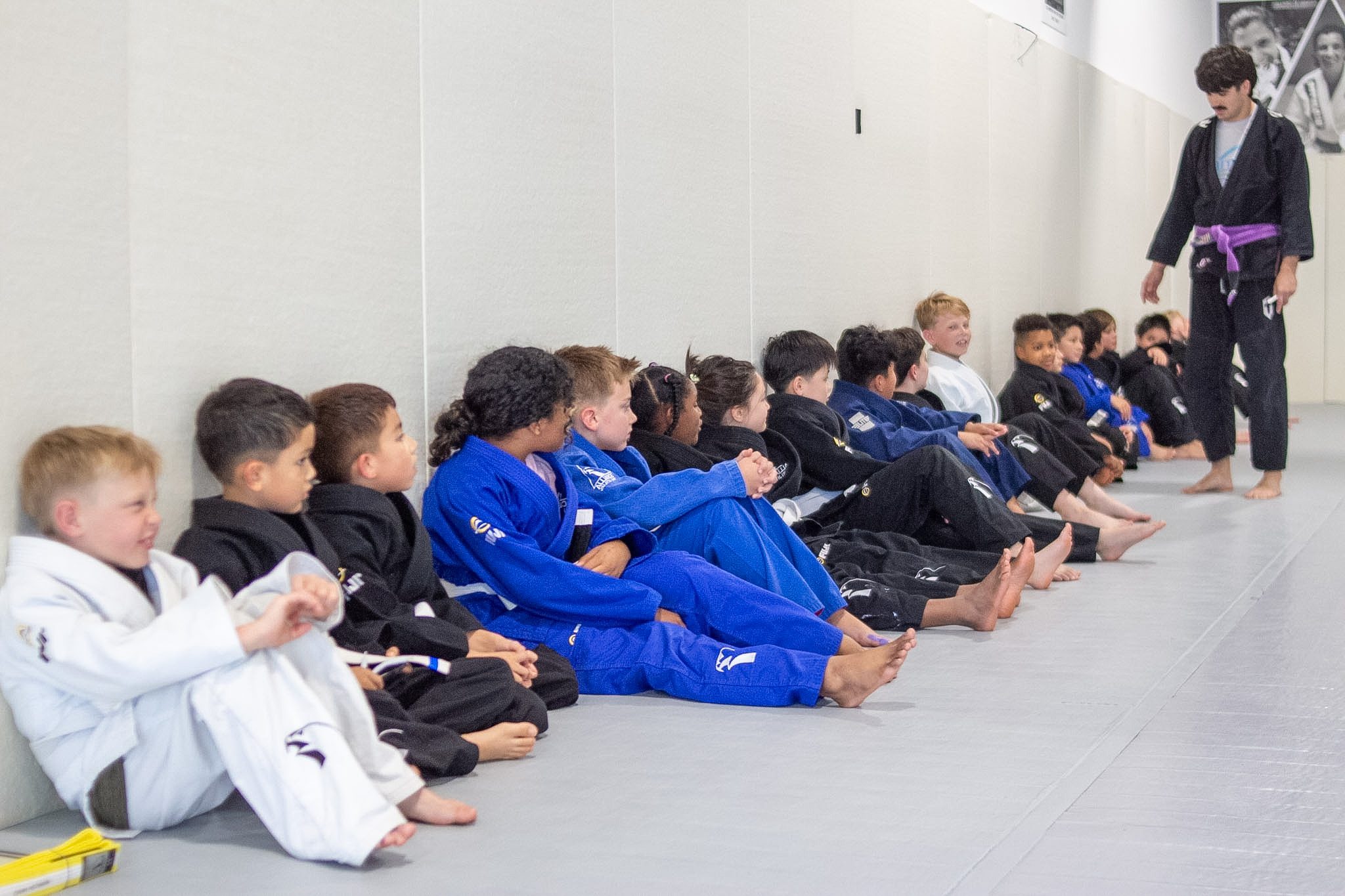 Alliance coach in black gi speaks to seated row of young students before promotion