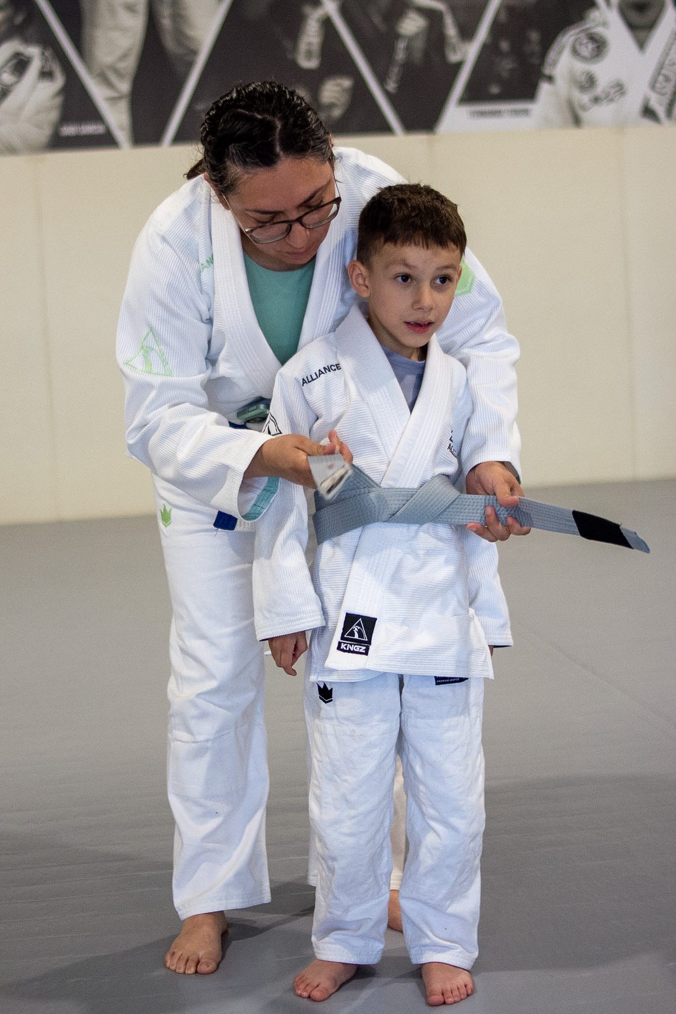 Female coach carefully ties a new grey belt around young student in white gi