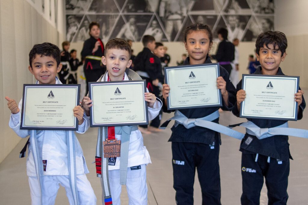 Four young Alliance students hold framed belt certificates after promotion ceremony