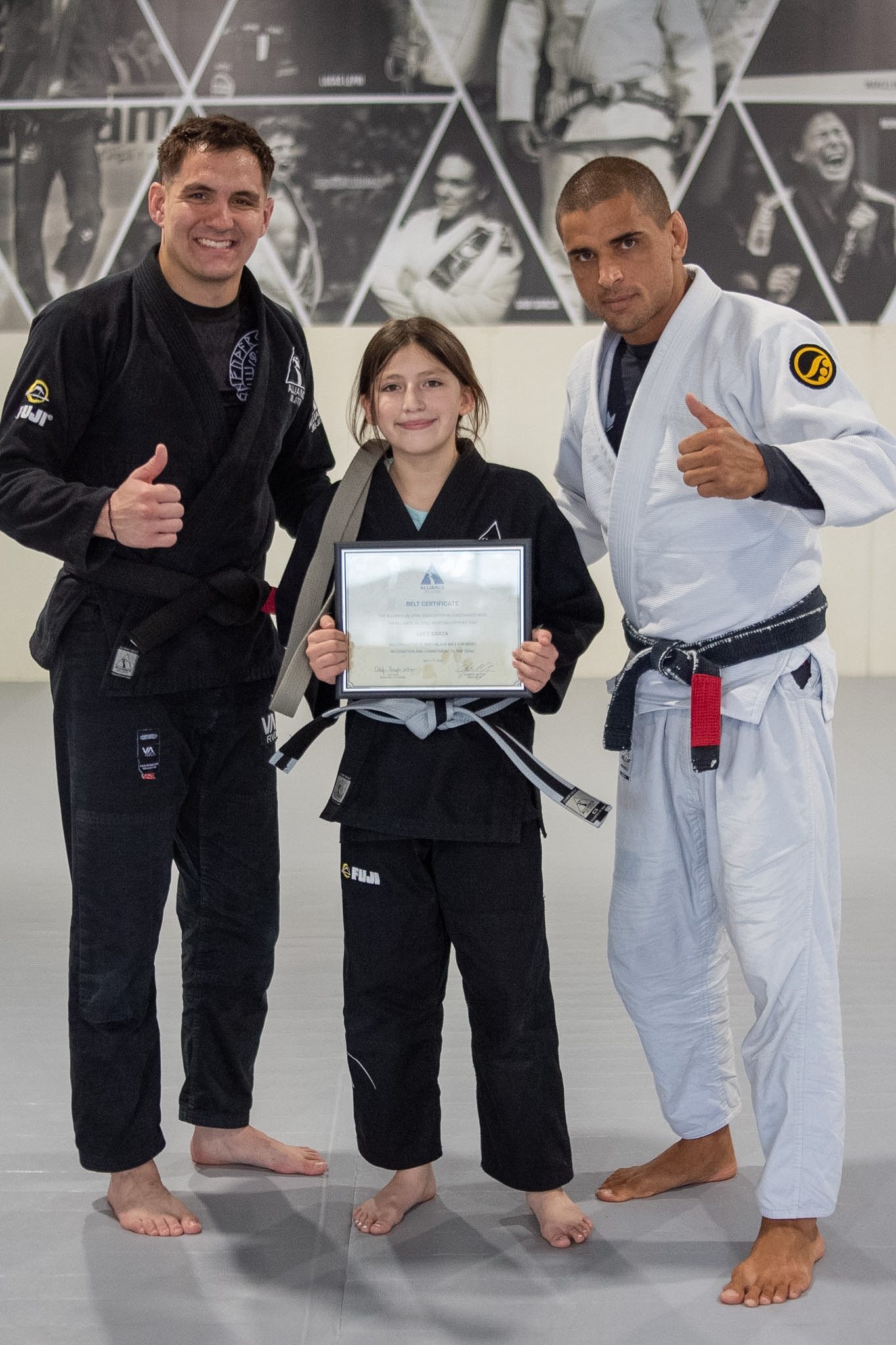 Young Alliance student with glasses holds belt certificate between two coaches
