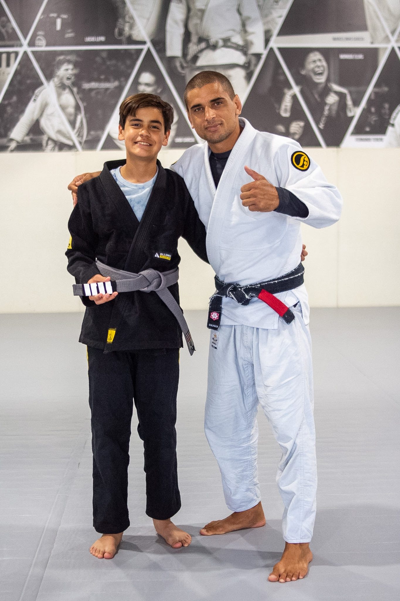 Junior Eagle in black gi holds new grey belt with head instructor