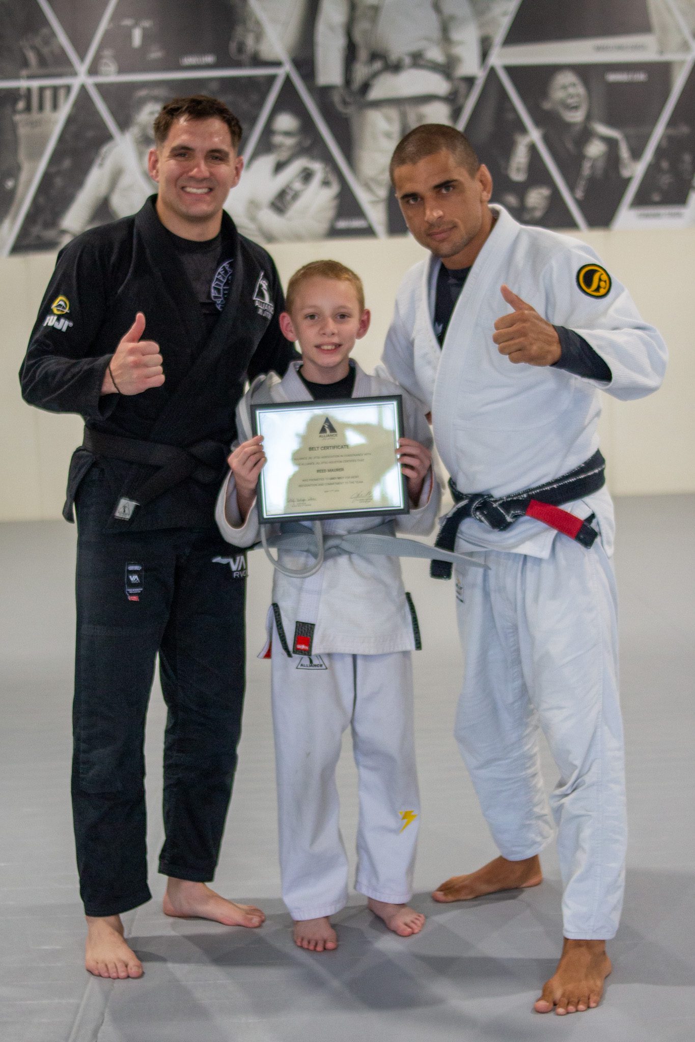 Junior Eagle in black gi with yellow belt holds Alliance promotion certificate
