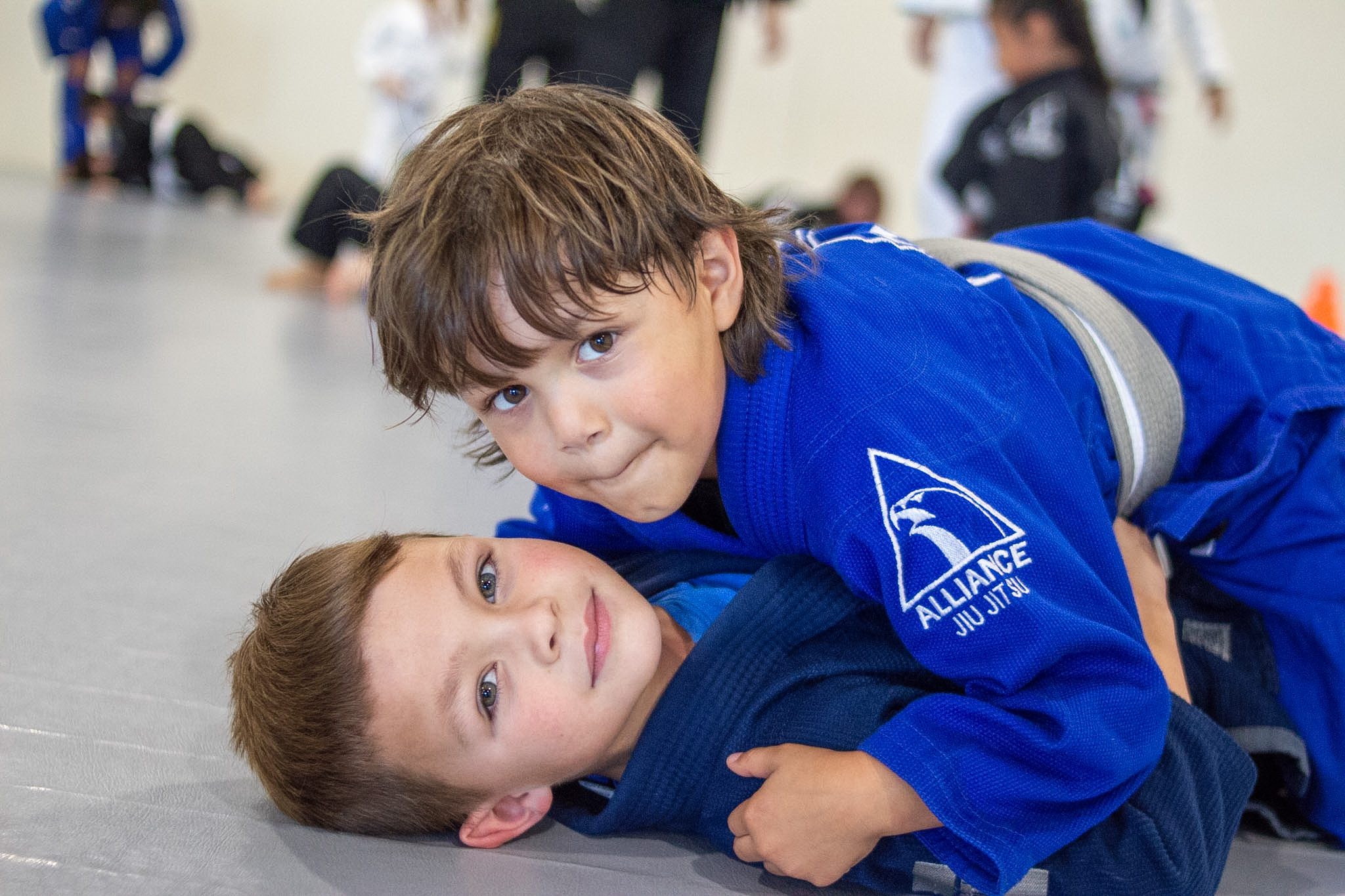 Two young students with grey-white belts drilling jiu-jitsu on the mat