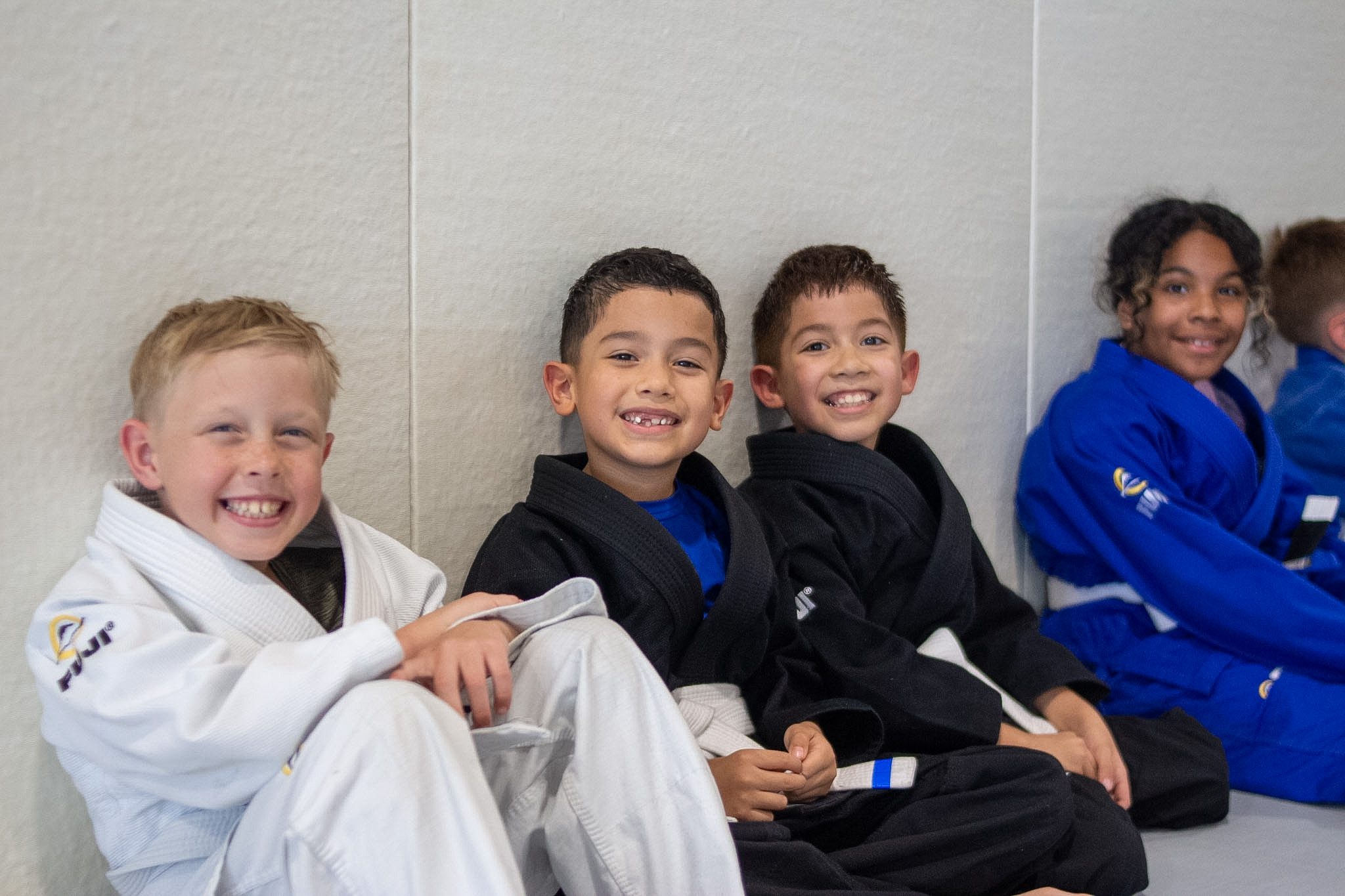 Row of young Alliance students sit along the wall waiting for belt ceremony