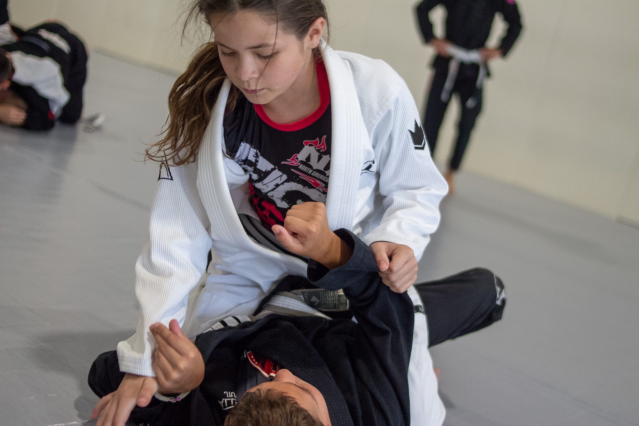 Two young students in dark gis practice standing takedown entries on the mat