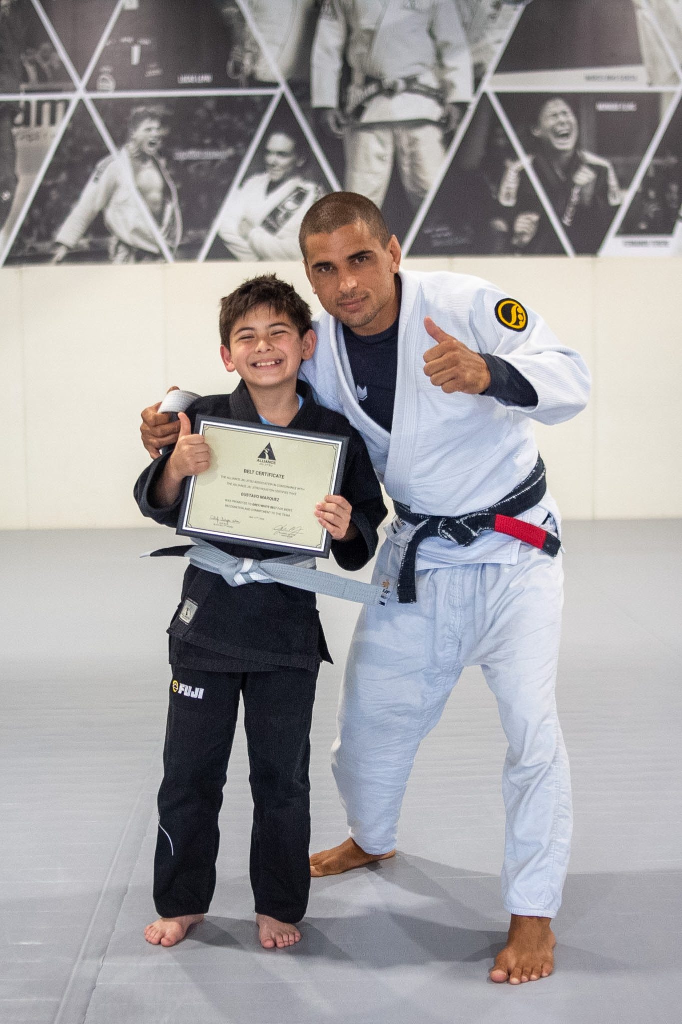 Smiling Little Eagle in black gi holds framed Alliance belt certificate