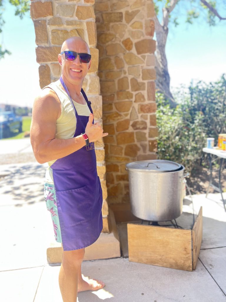 Coach Tony Landry in purple apron next to giant crawfish pot throwing a shaka