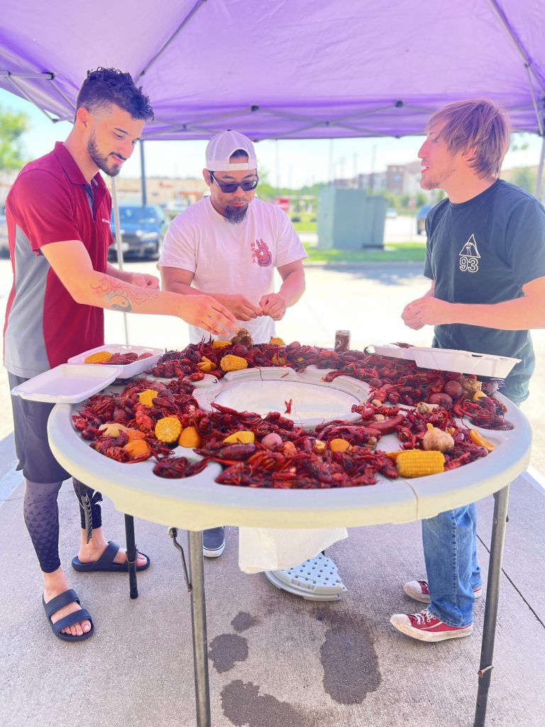 Three members gathered around large round table piled with crawfish corn and potatoes
