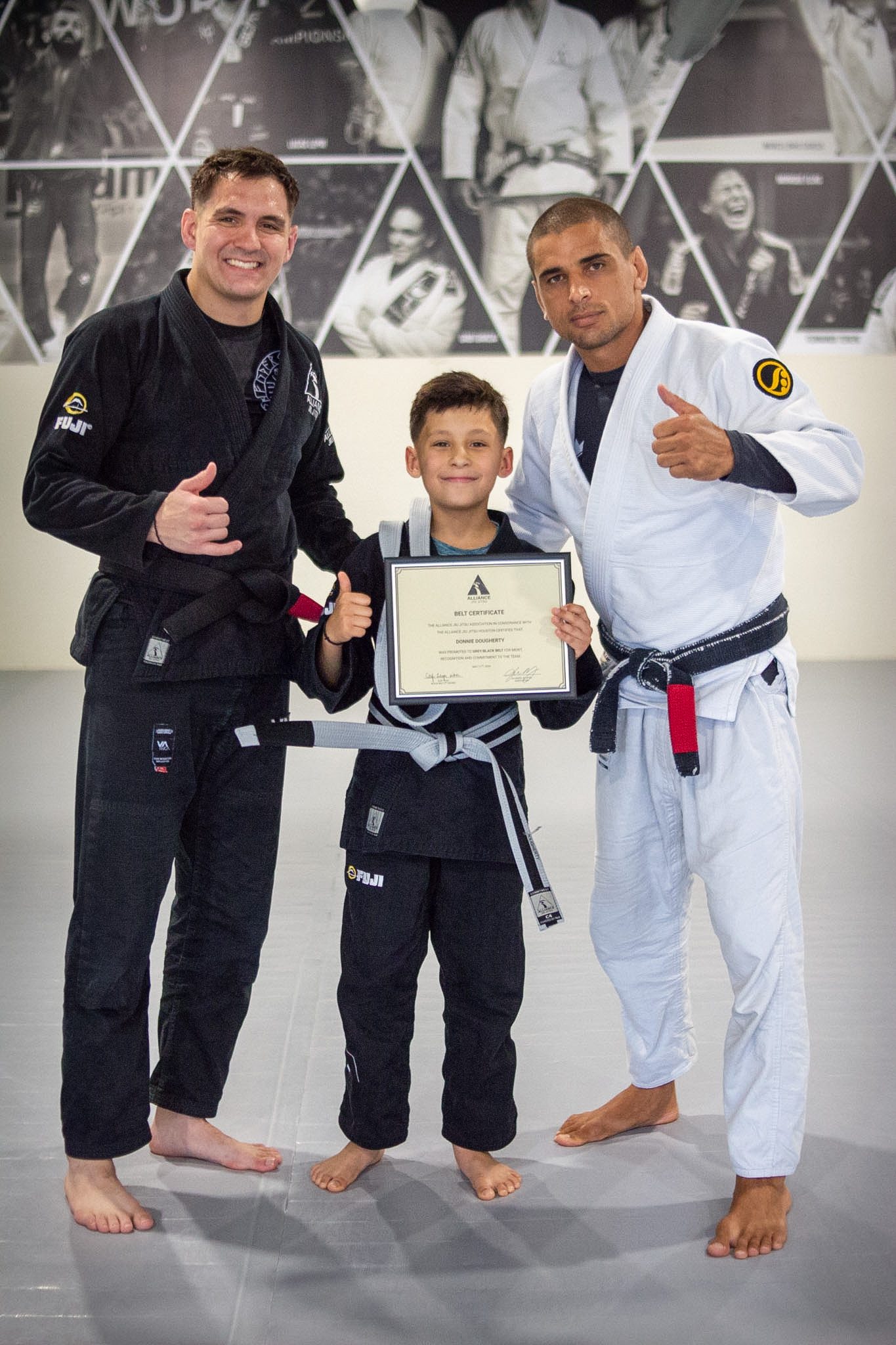 Young female Alliance student holds belt certificate between two coaches