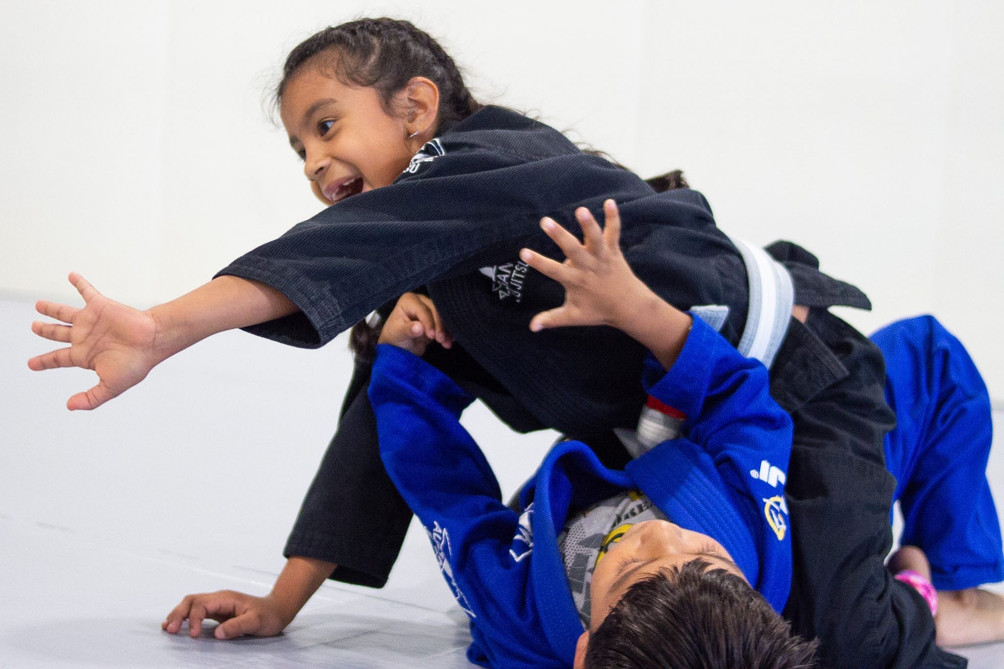 Smiling young girl in black gi establishing top position over training partner