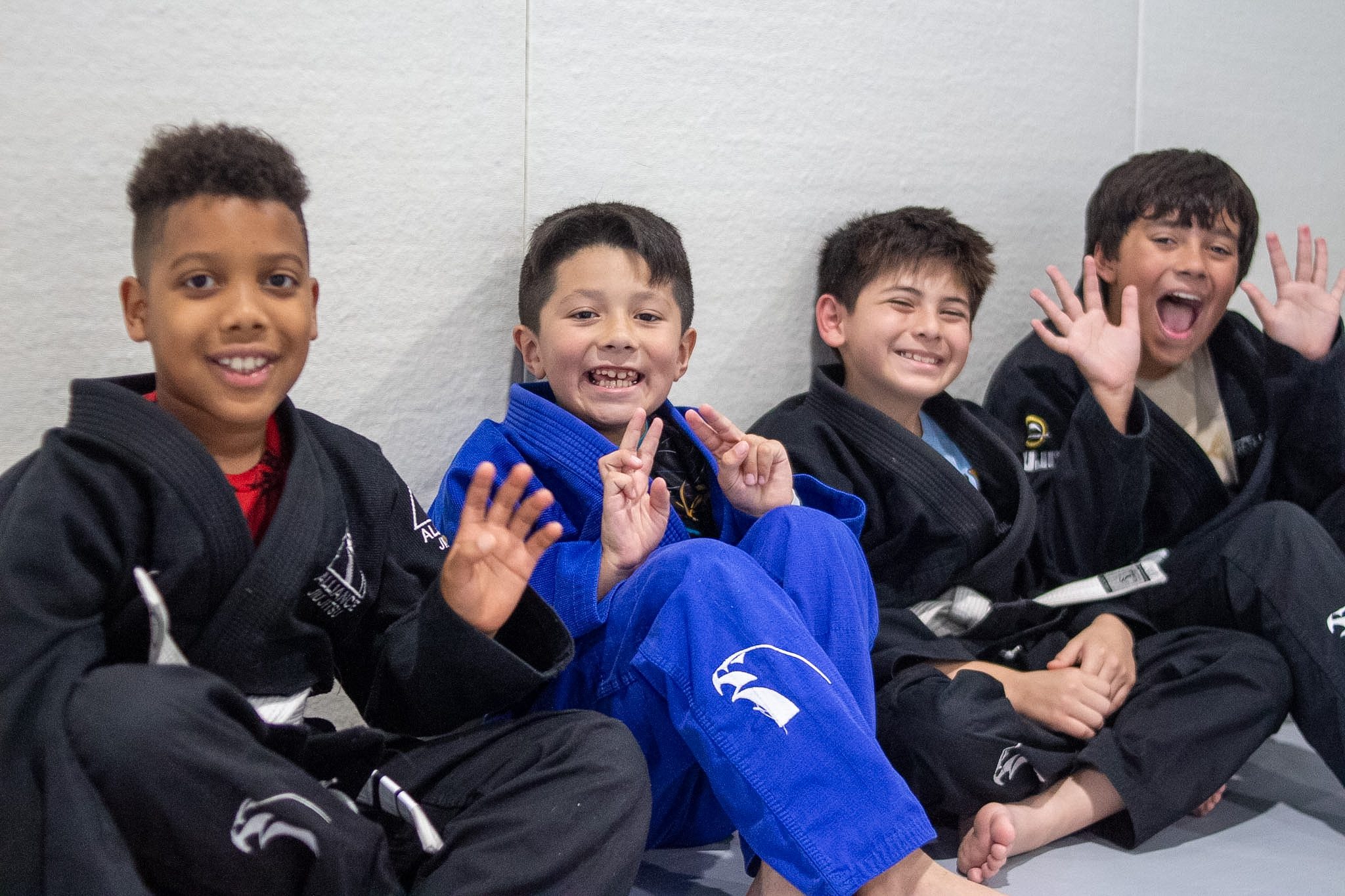 Older student in white gi controls top mount during kids jiu-jitsu sparring round