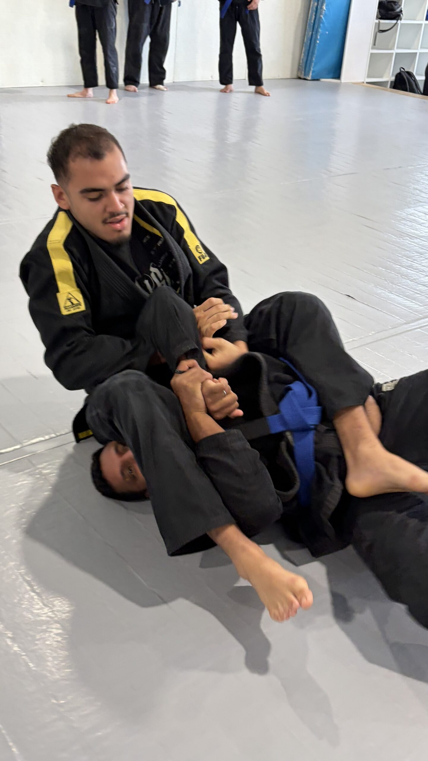 Grappler in a black gi works a leg lock on a partner lying on the mat