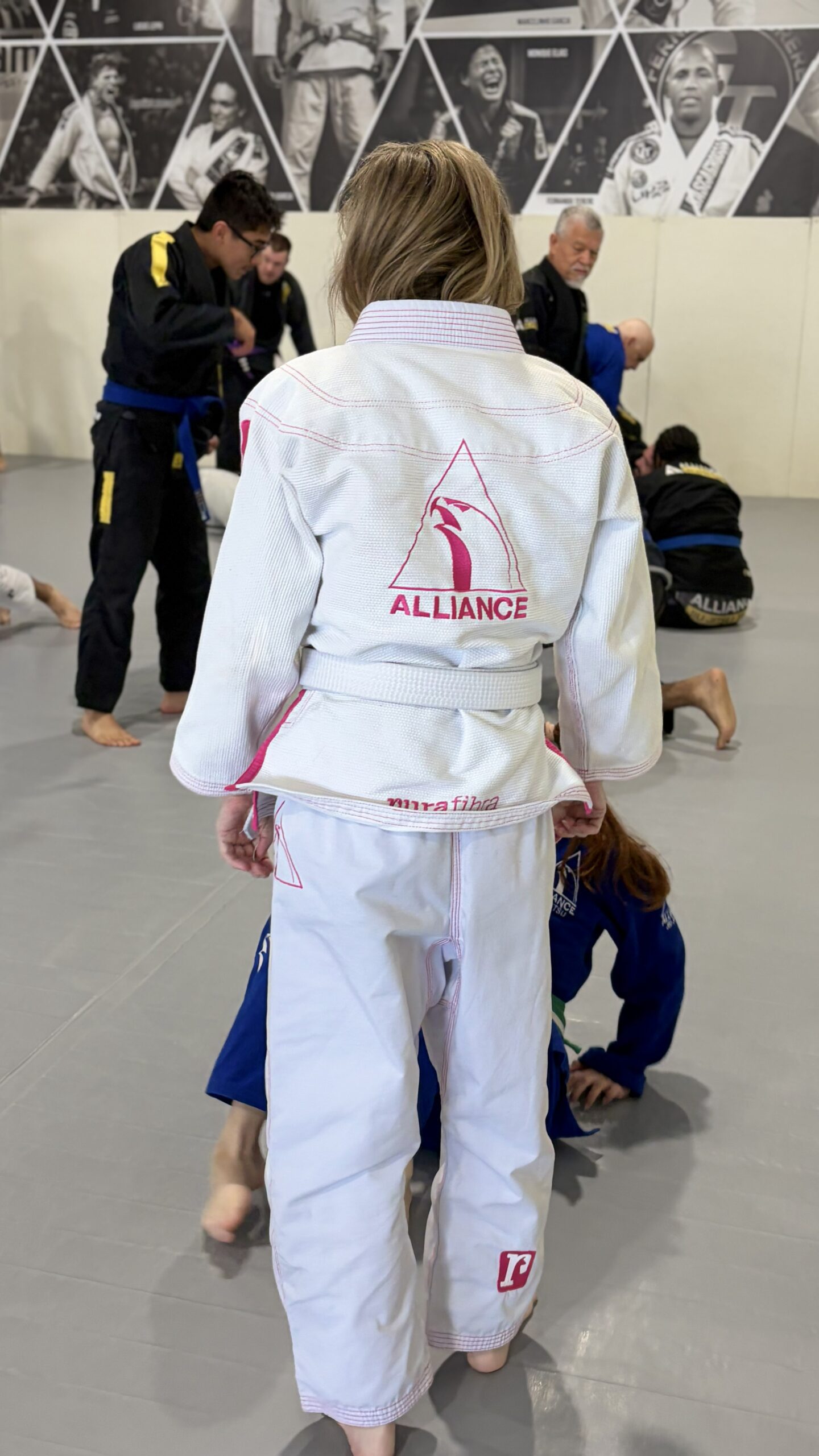 Blonde woman in a white gi faces off with training partners during adult open mat