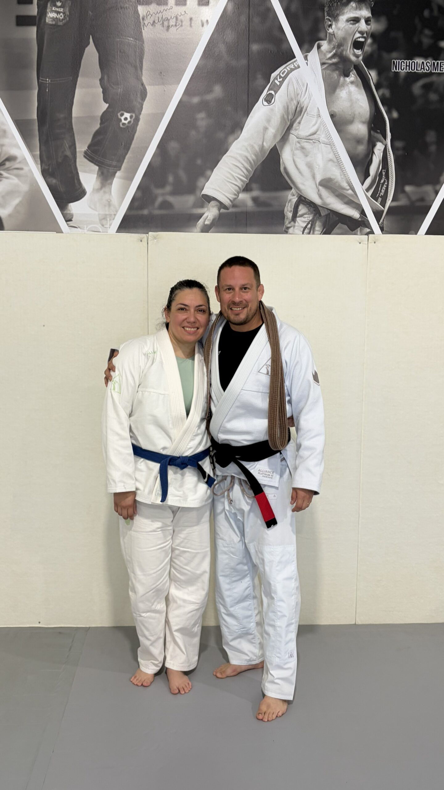 Woman in a white gi with a new blue belt poses arm-in-arm with her coach