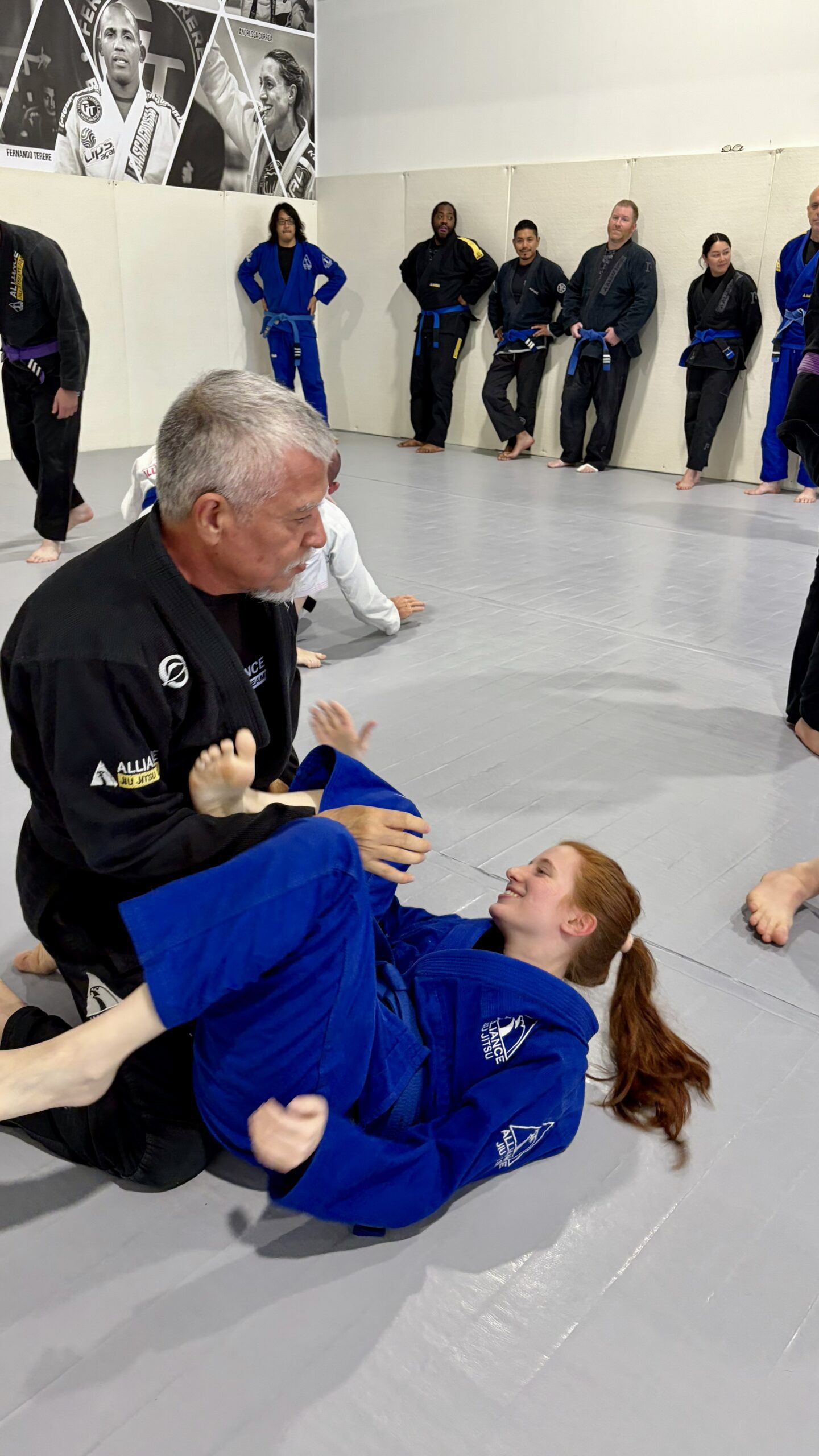 Older man in a black gi rolls with a younger partner during open mat
