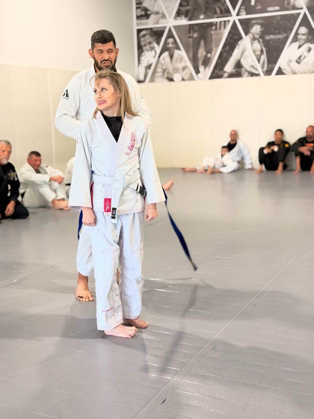 Blonde woman in a white gi stands with a bearded Alliance coach during her promotion