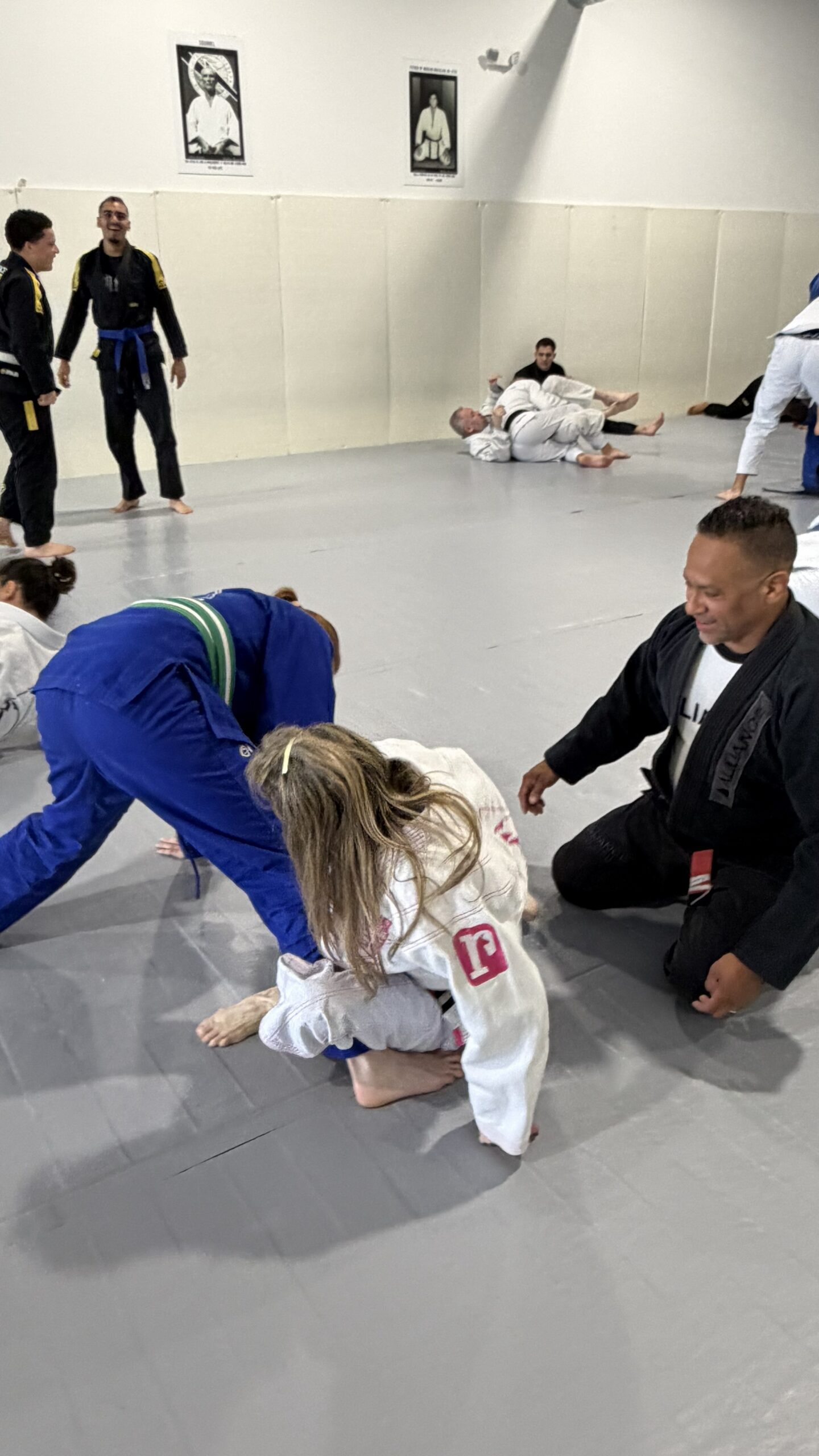 Young child in a white gi plays near a smiling coach during a relaxed mat moment