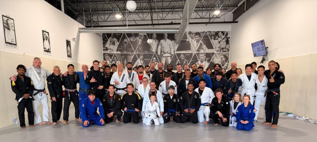 Around forty adult students and coaches gather on the mat after Alliance belt promotions