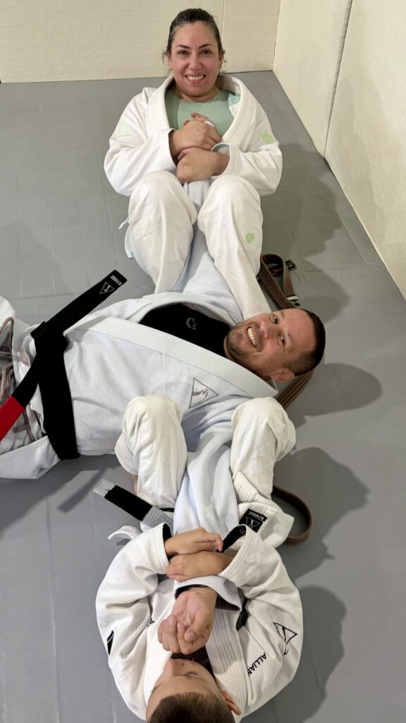 Black belt in a white gi laughs on the mat with teammates during a light moment