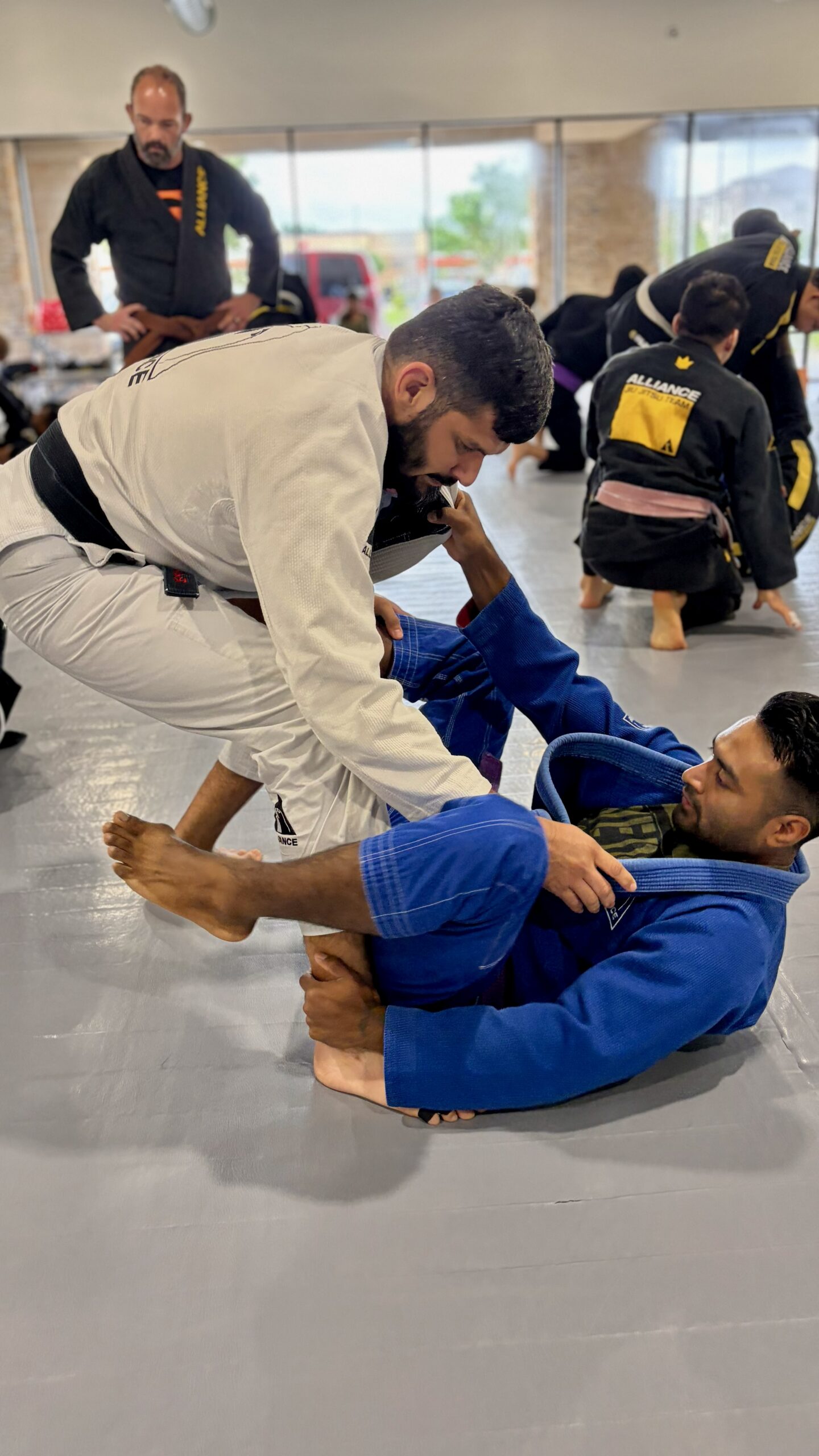 Black belt in a white gi passes a partner's guard during adult class