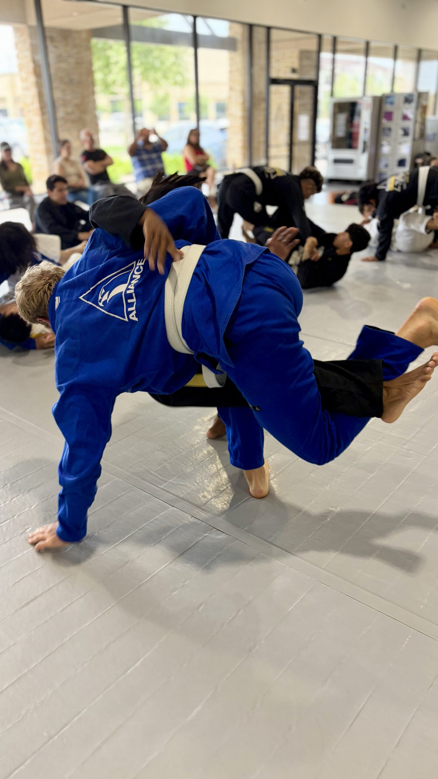 Man in a blue gi lands a takedown on a partner during a packed open mat