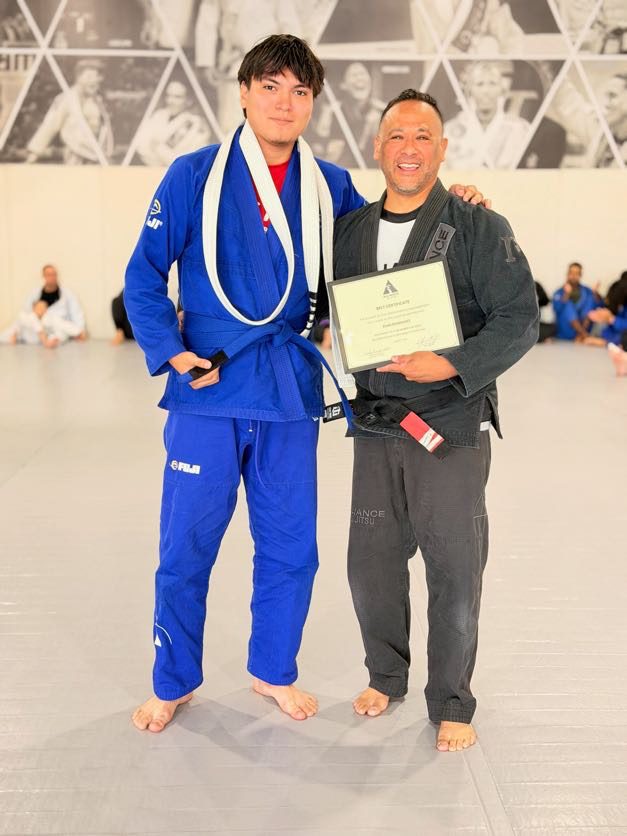 Man in a blue gi holds his certificate and new blue belt