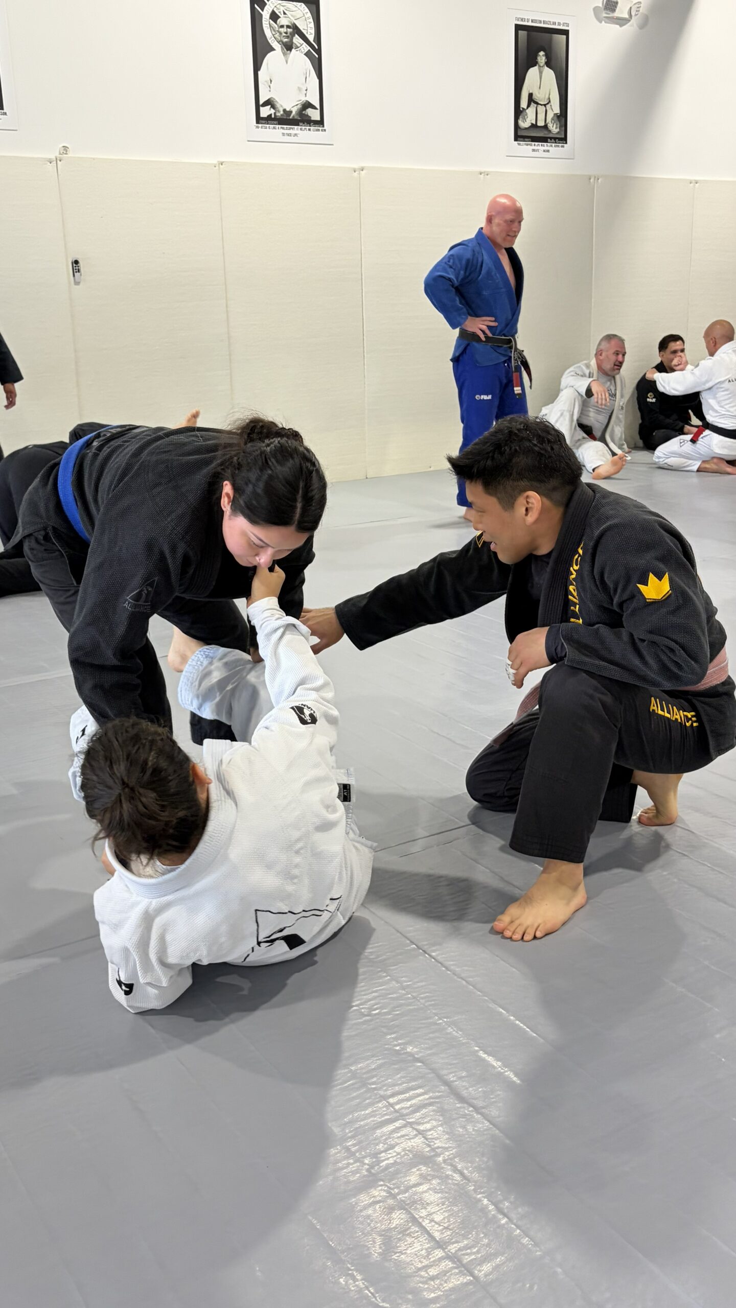 Woman in a black gi rolls with a child in a white gi on the mat