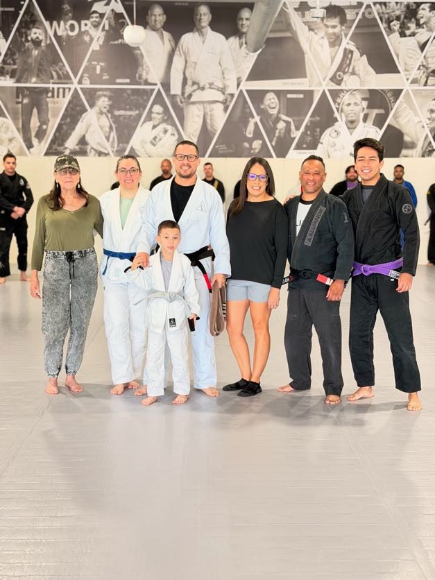 Jason Quilantan wears his new black belt surrounded by family on the Alliance mat